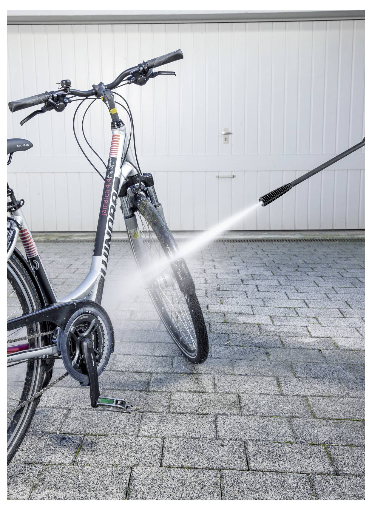 En cykel som rengörs med en högtryckstvätt, med fokus på framhjulet och ramen, placerad framför en garageportsbakgrund.