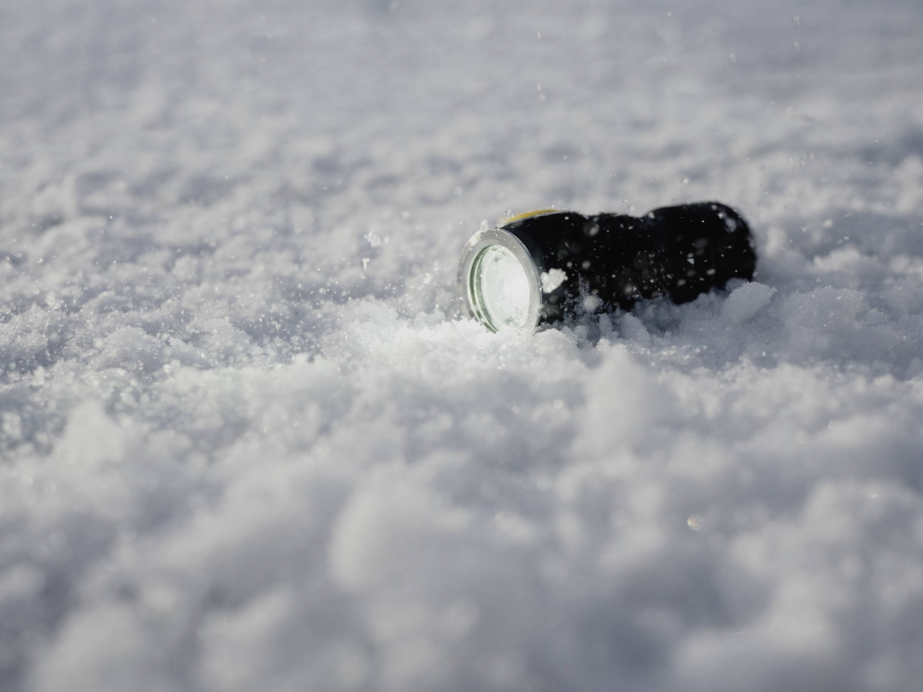 Ficklampa liggande i snön vid dagsljus, omgiven av fallande snöflingor.