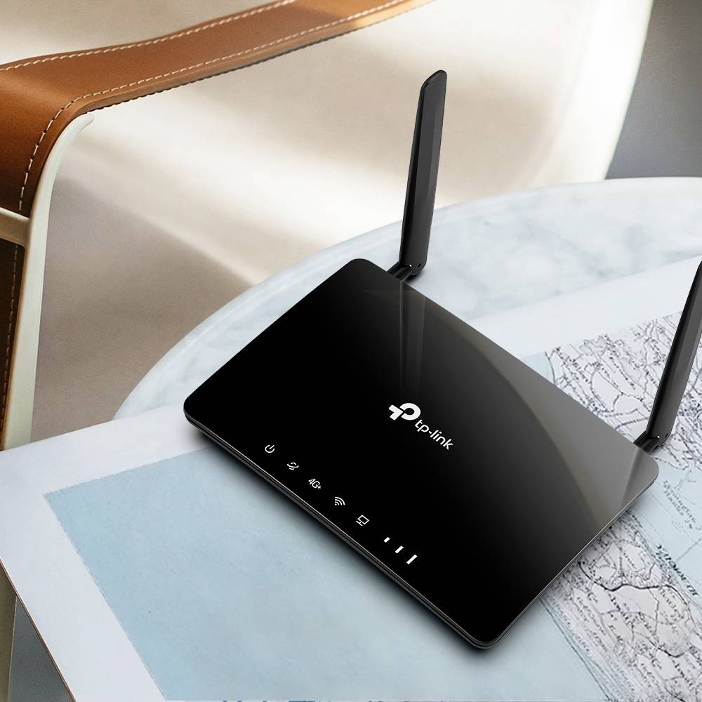 En svart router med två antenn på ett bord bredvid ett kort. TP-Link-logotypen syns på ovansidan.