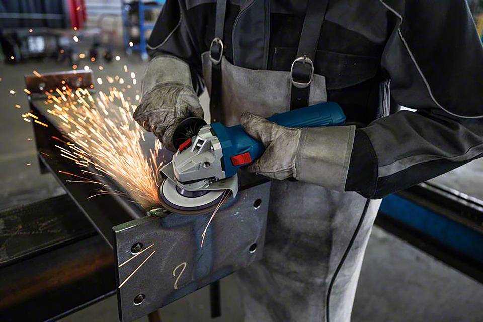En person sliper ett metallstycke med en vinkelslip. Gnistor sprider sig från metallen. Personen bär skyddsutrustning.