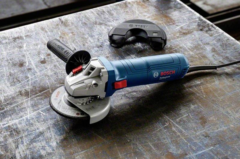 En blå Bosch-vinkelslipmaskin ligger på ett slitet metallbord. Bredvid den ligger ett skyddslock.