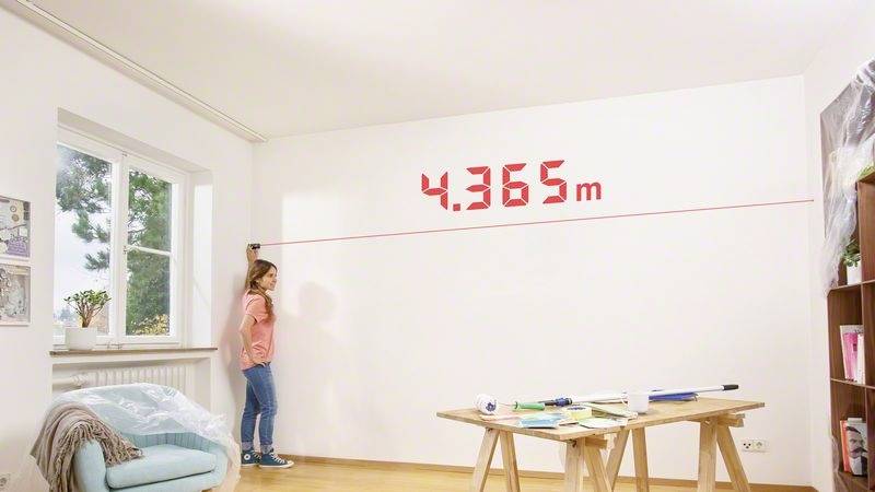 En flicka mäter väggens bredd med en lasermätare, displayen visar '4,365 m'. I rummet finns möbler och ett fönster.