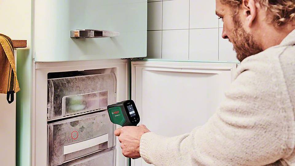 En man använder ett infraröd termometer för att mäta temperaturen i frysskåpet. Frysskåpet är öppet och förfruset.