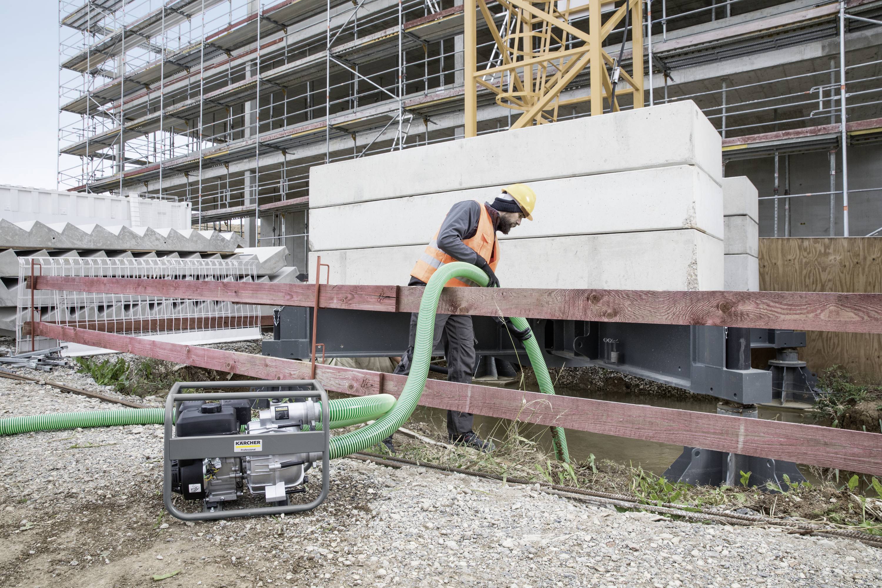 En byggnadsarbetare pumpar vatten på en byggarbetsplats. I bakgrunden syns ställningar och betongblock.