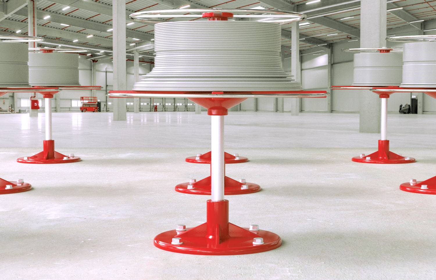 Stora röda spolar med grå kabel utplacerade jämnt på golvet i en industrihall. Taket har synliga ventilationsrör.