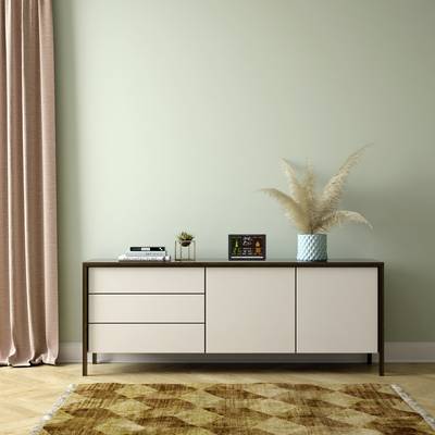 En modern byrå står framför en grön vägg med en växt, en väckarklocka och en bok på sig. Bredvid hänger en beige gardin.