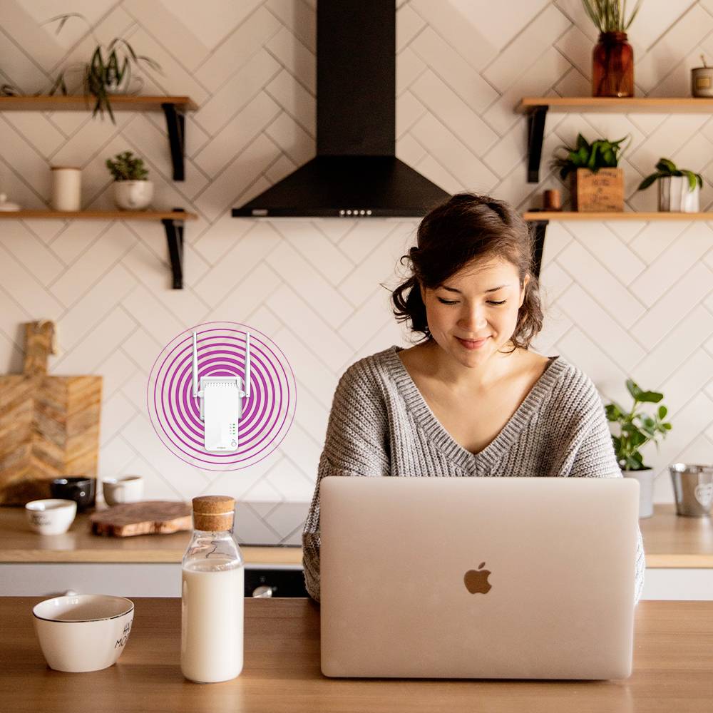 En kvinna arbetar på en bärbar dator i ett modernt kök och ler. Bredvid henne svävar en router-symbol som antyder ett trådlöst nätverk.