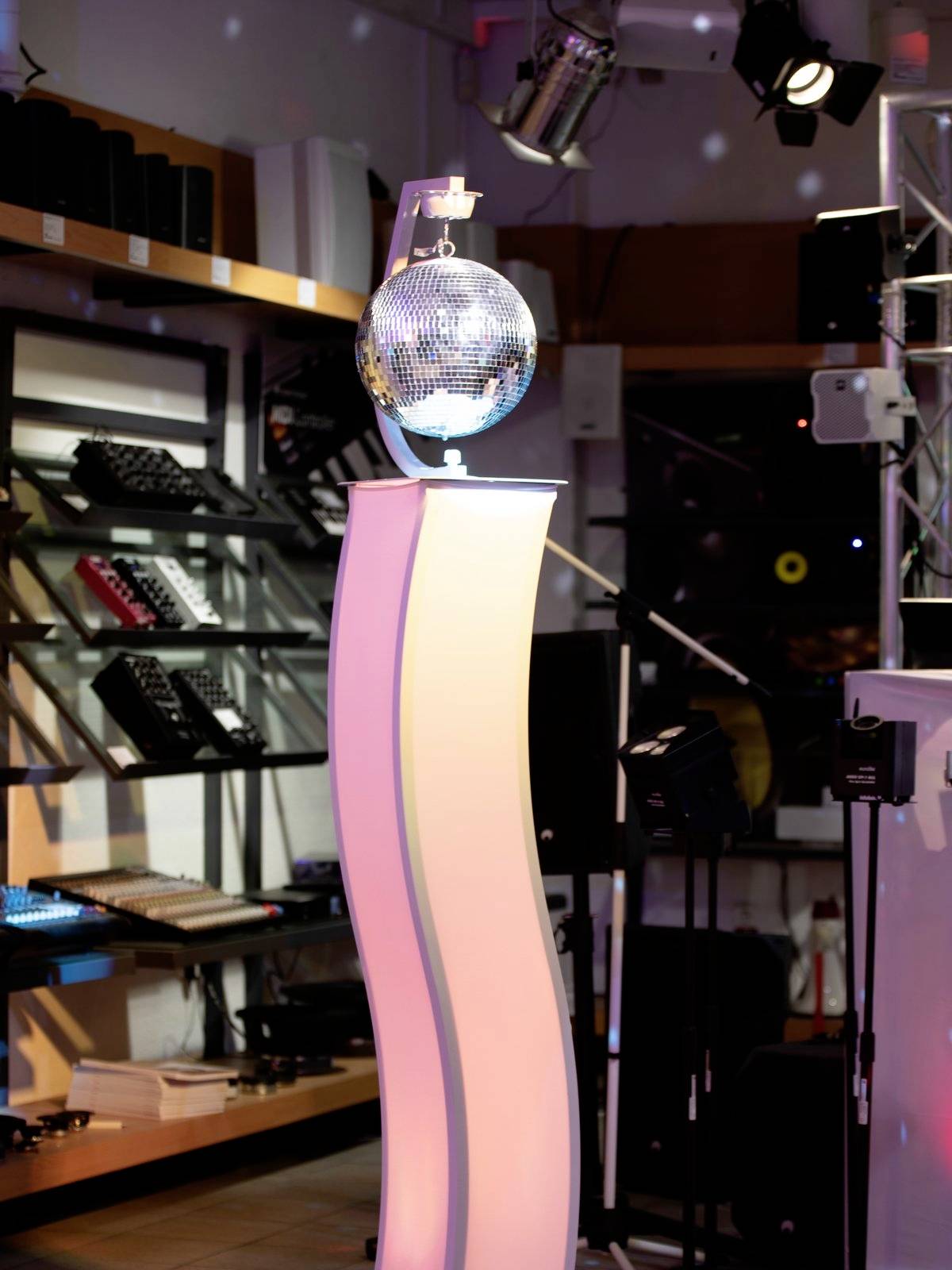 En belyst piedestal i en musikaffär visar en glänsande discobal. I bakgrunden syns musikinstrument och högtalare.