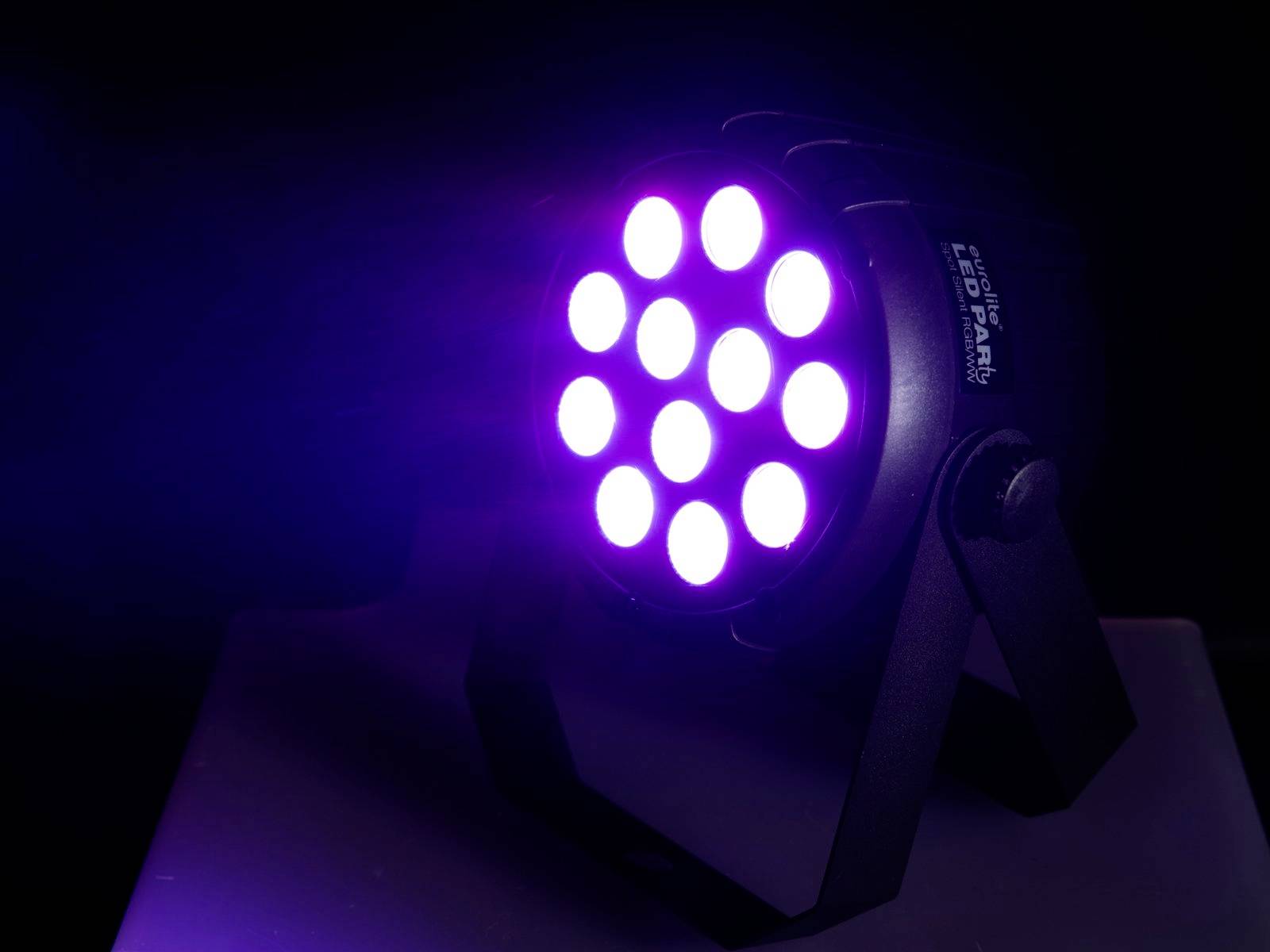 En LED-ljusstrålkastare lyser med violett ljus i ett mörkt rum. Strålkastaren har runda linser, arrangerade i ett gittermönster.