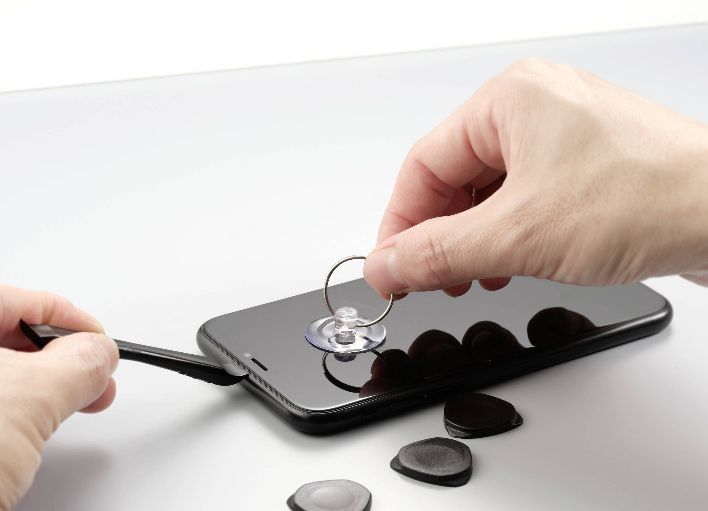 Två händer reparerar en smartphoneskärm med ett sugverktyg och en hävstång för att lyfta skärmen.