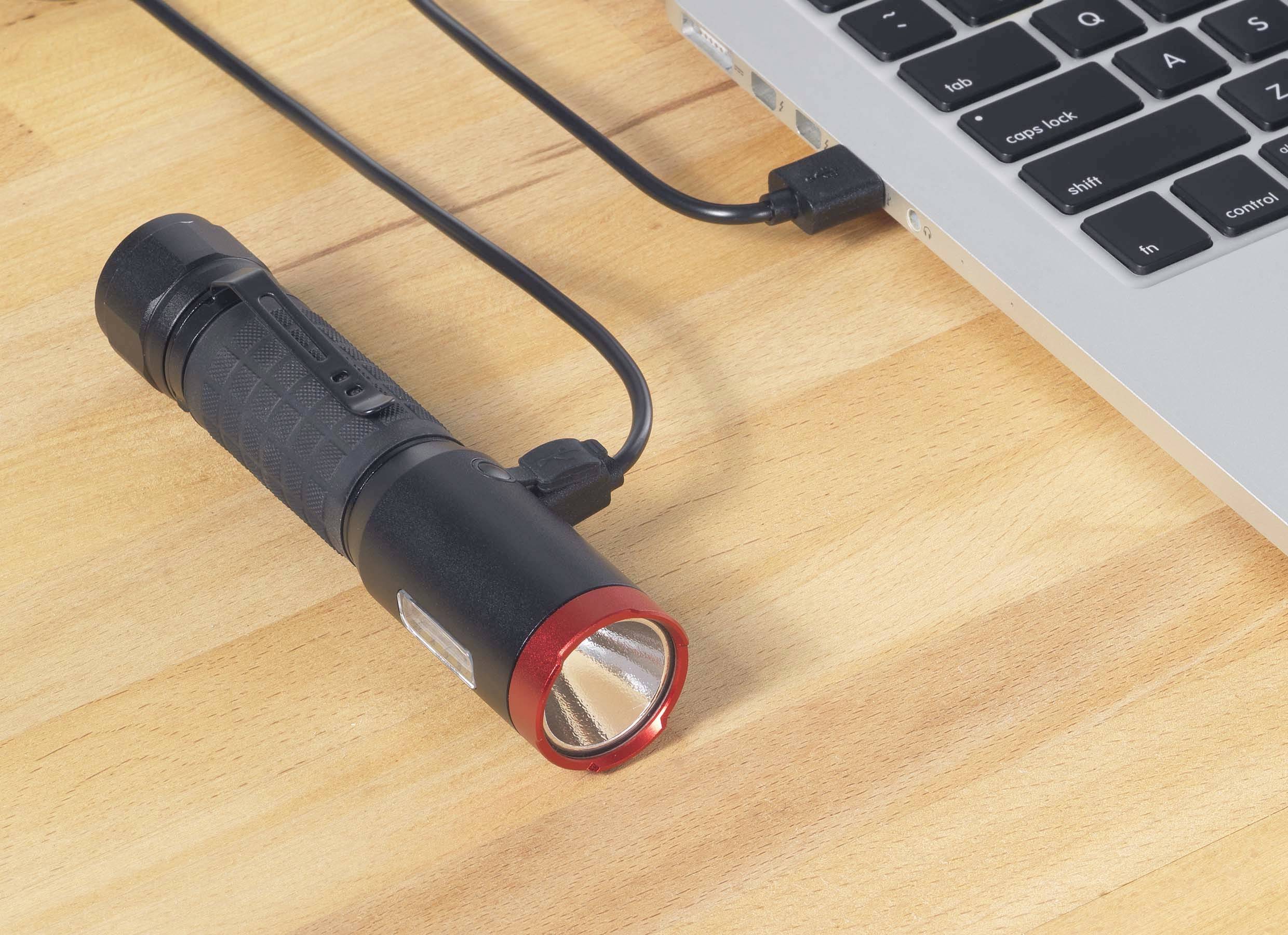 Ficklampa med röd kant laddas medan den är ansluten till en bärbar dator via en USB-kabel.