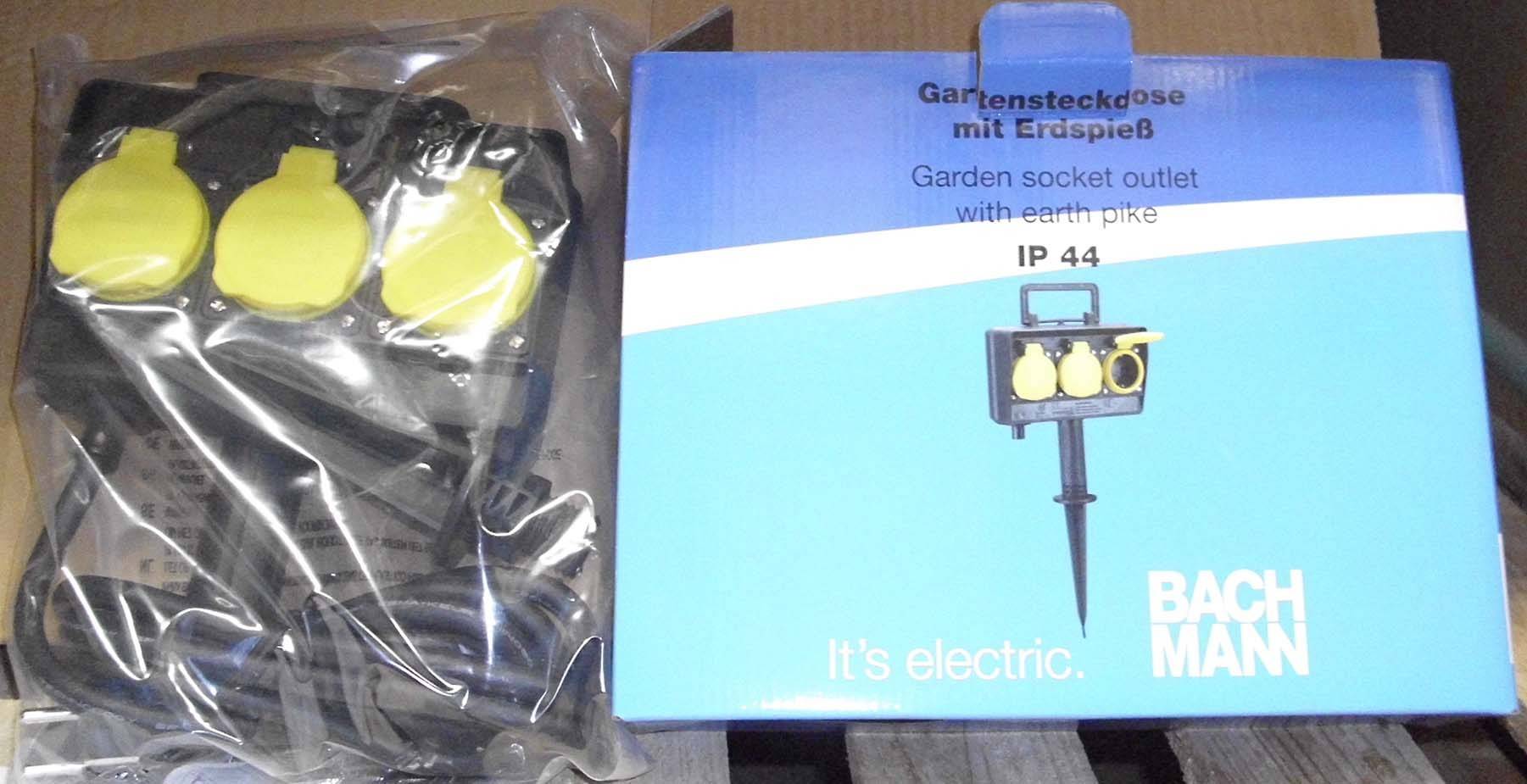 Förpackning till en trädgårdsuttag med jordspett, Bachmann, modell IP 44. Innehåller tre gula anslutningsplatser. Förpackningsetikett: "It's electric".