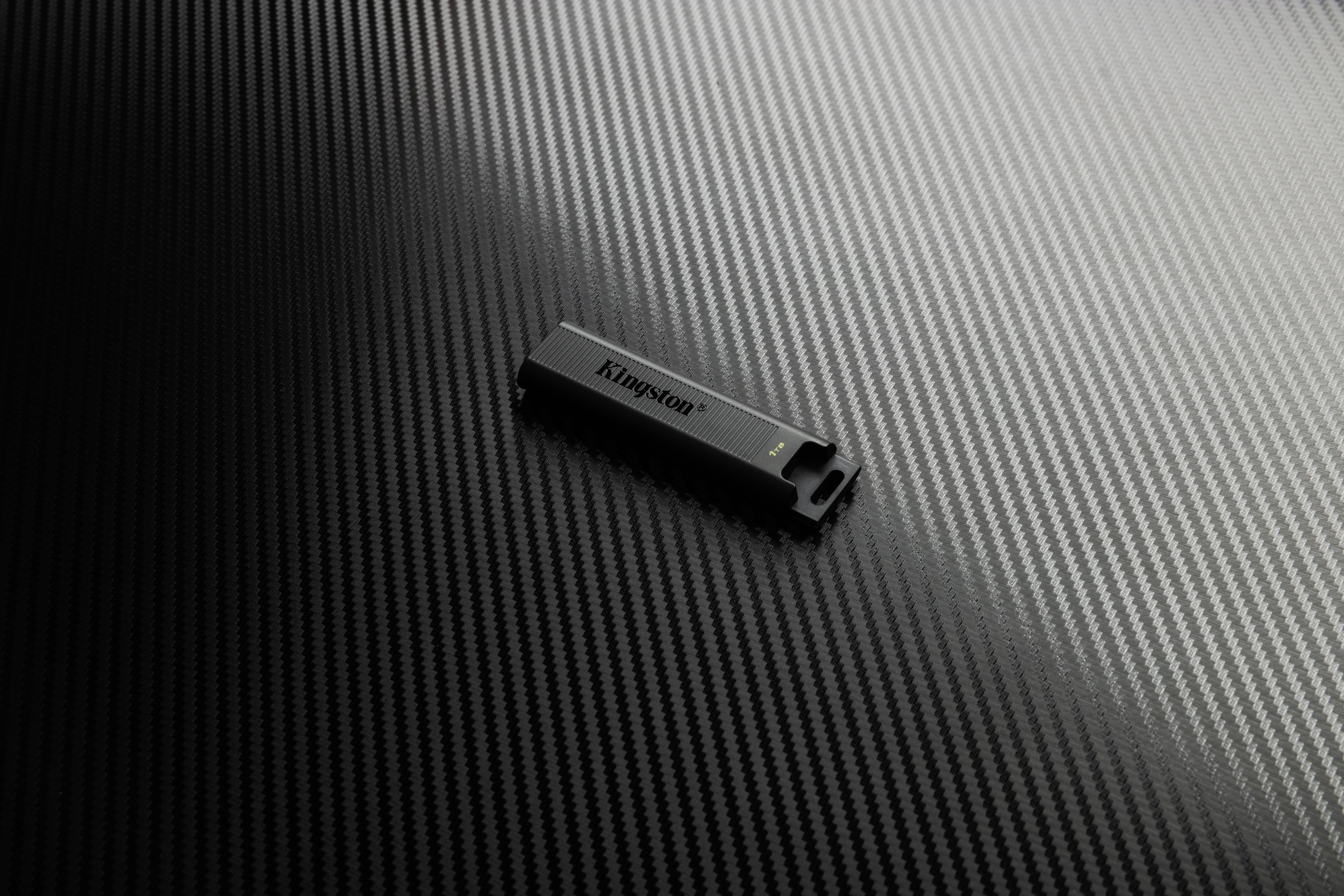 En svart USB-sticka ligger på en yta med kolfiberstruktur.