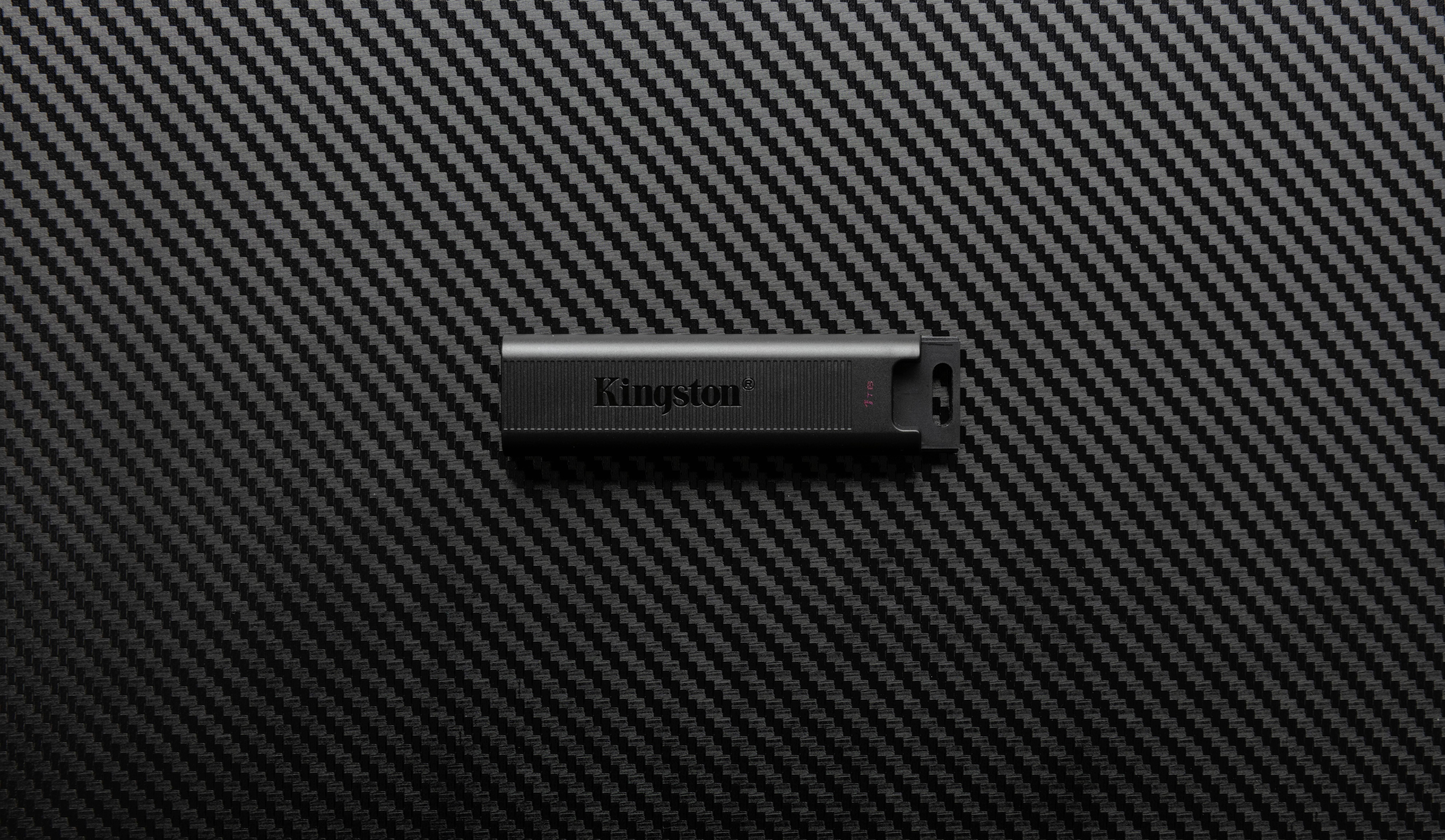 En svart USB-sticka från märket Kingston ligger på ett strukturerat, kolfiberliknande underlag.