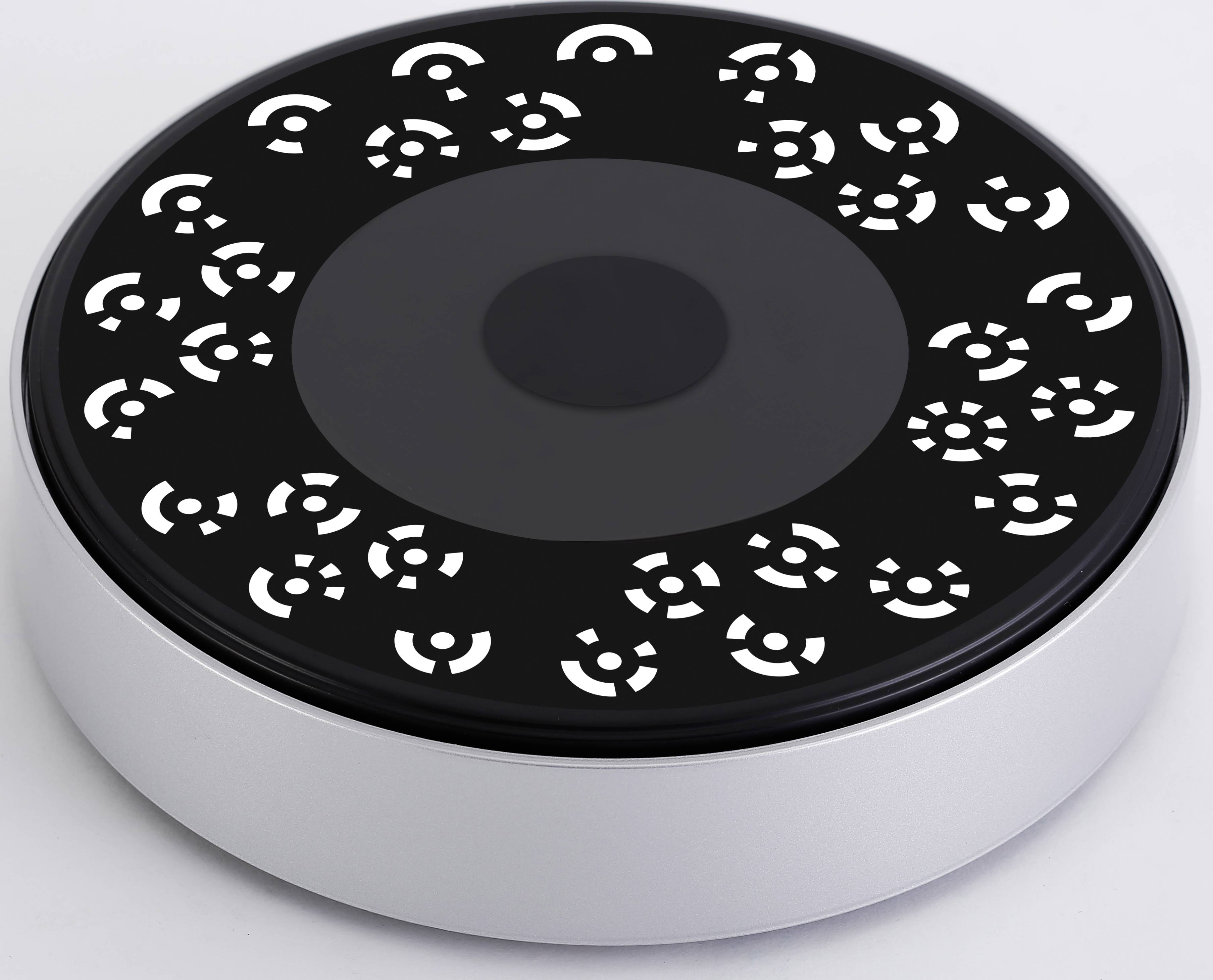 En rund, silverfärgad apparat med svart yta och vita cirkelformade mönster. Kan eventuellt användas för belysning eller dekoration.