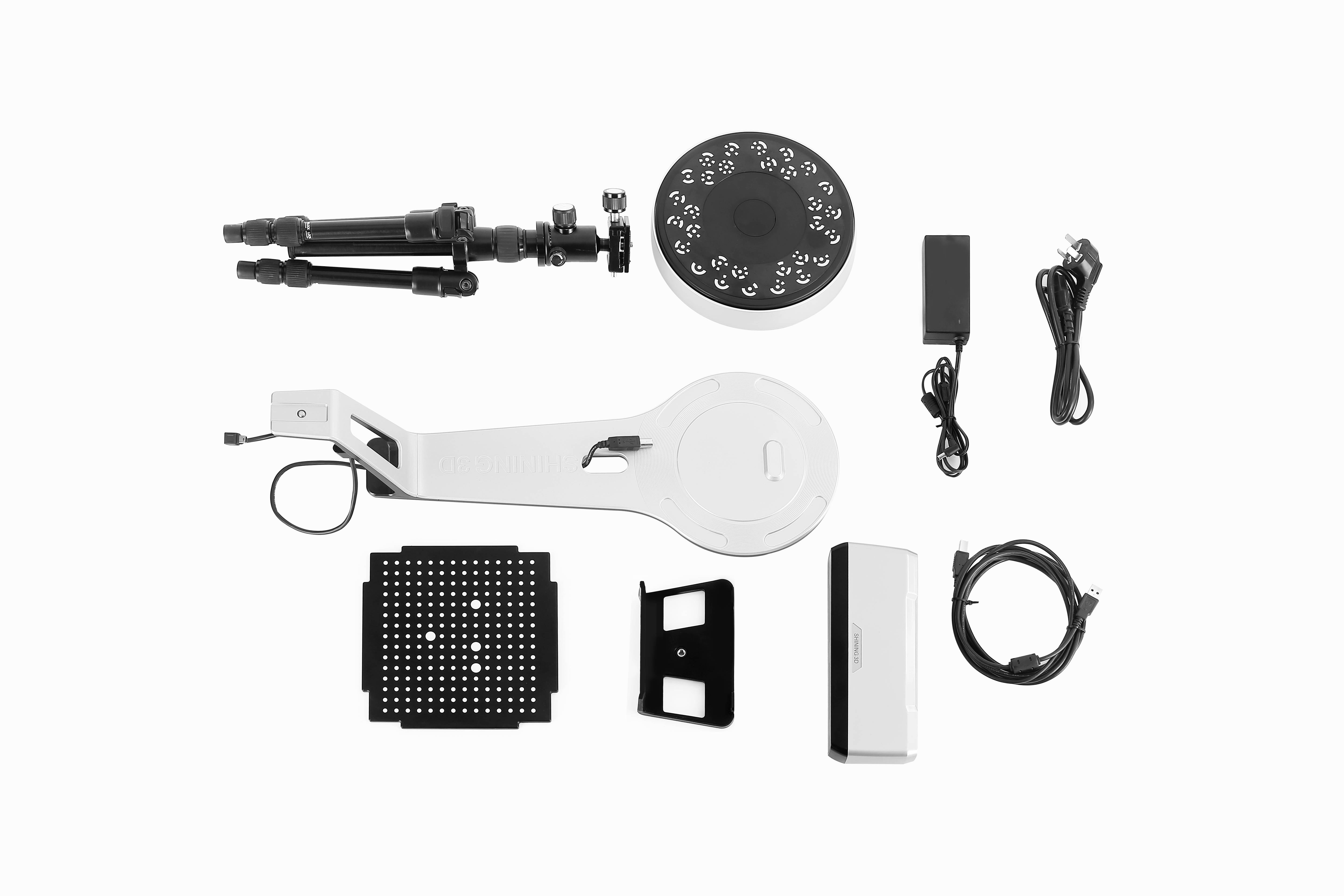 3D-skannerkomponenter på vit bakgrund: stativ, roterande plattform med punktmönster, nätadapter, kabel, fästen.
