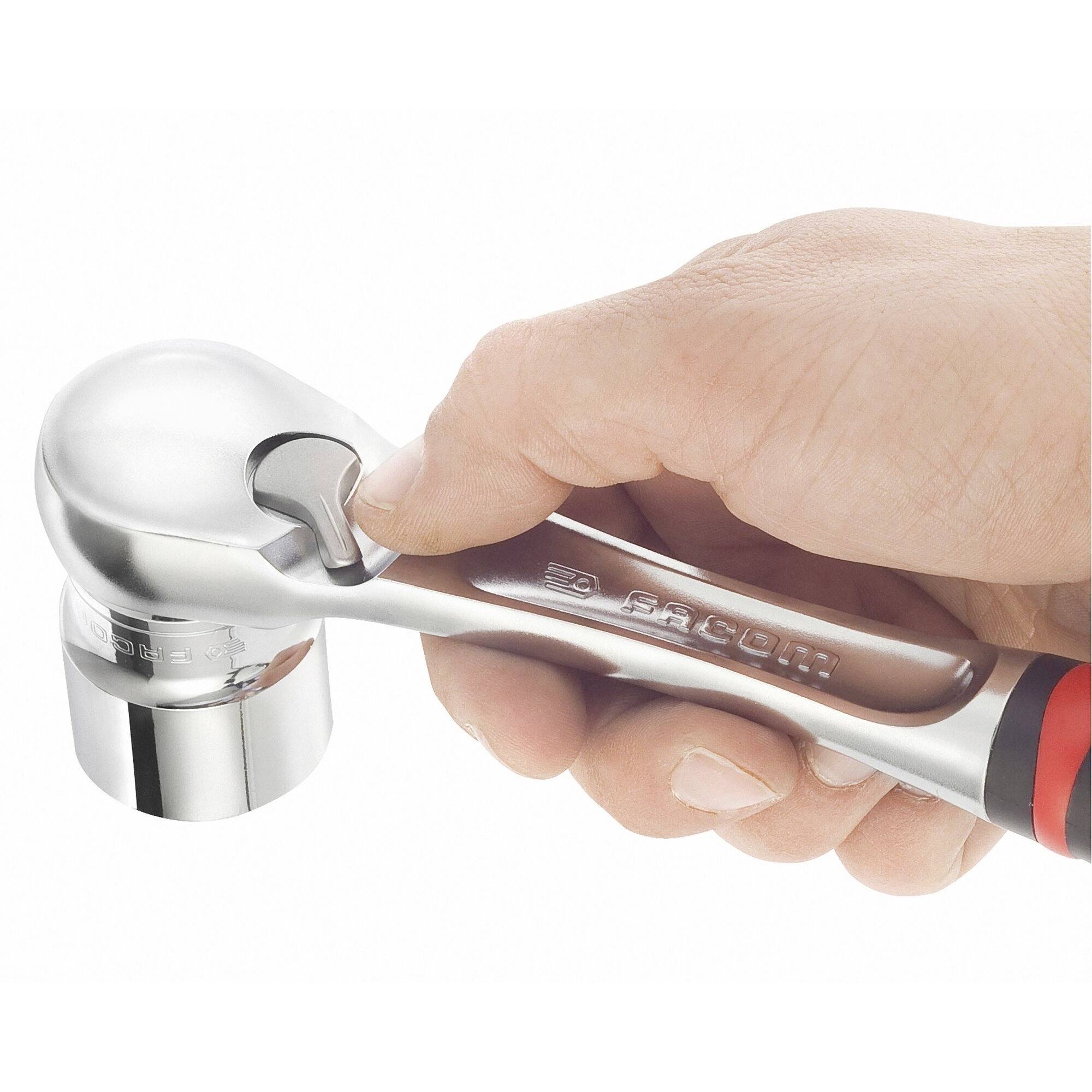En hand håller en silverfärgad skiftnyckel. Fokus ligger på det ergonomiska greppet och det anslutna tillbehöret.