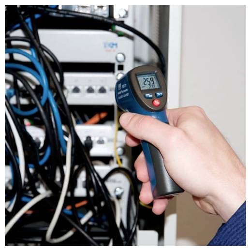Hand som håller en digital infraröd termometer riktad mot elektrisk utrustning och trassliga kablar inuti ett skåp.