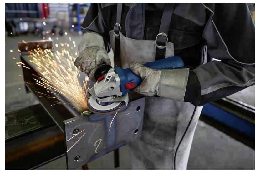 Arbetare som sliper metall med en vinkelslipar och producerar ljusa gnistor i en industriell verkstad.