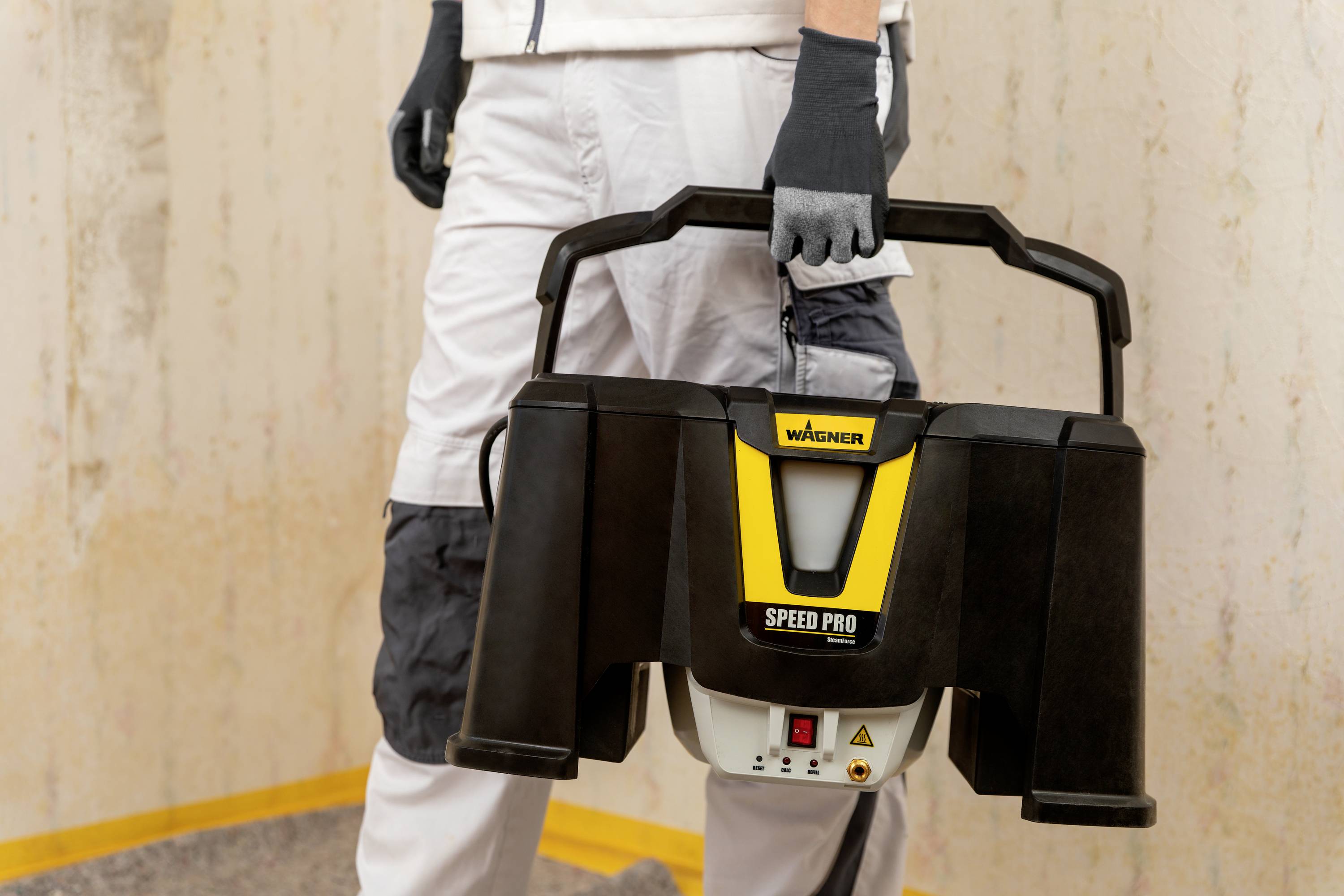 En person håller en svart apparat märkt 'Wagner Speed Pro'. Enheten ser funktionell ut och kan vara avsedd för hantverksarbeten.