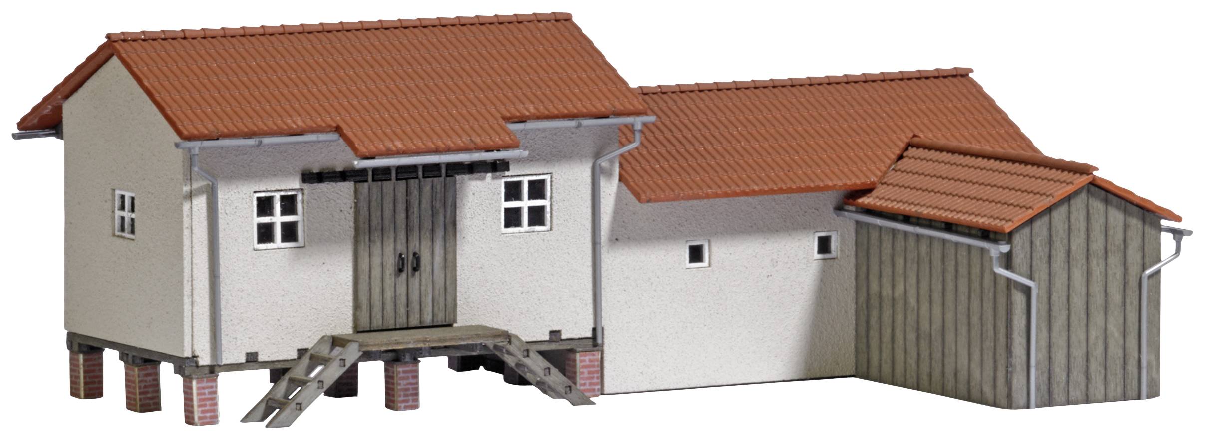 En liten modellbyggnad med röda tegeltak och detaljerad trappa. Byggnaden höjer sig lätt över marken på träpålar.