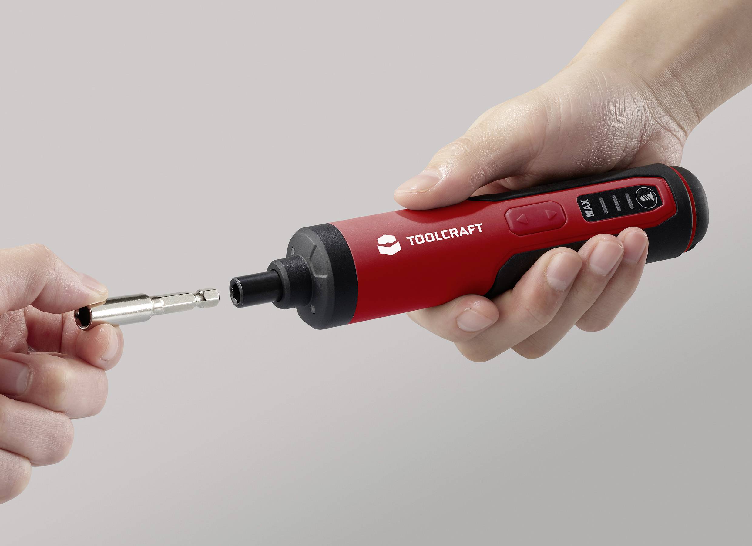 En hand håller en röd, sladdlös skruvmejsel märkt 'TOOLCRAFT'. En annan hand håller en matchande bits framför den.