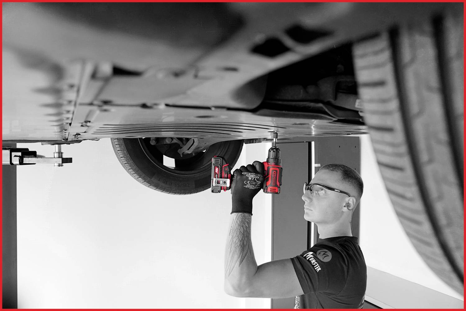 En mekaniker lyfter en bil och arbetar med ett elverktyg på undersidan.