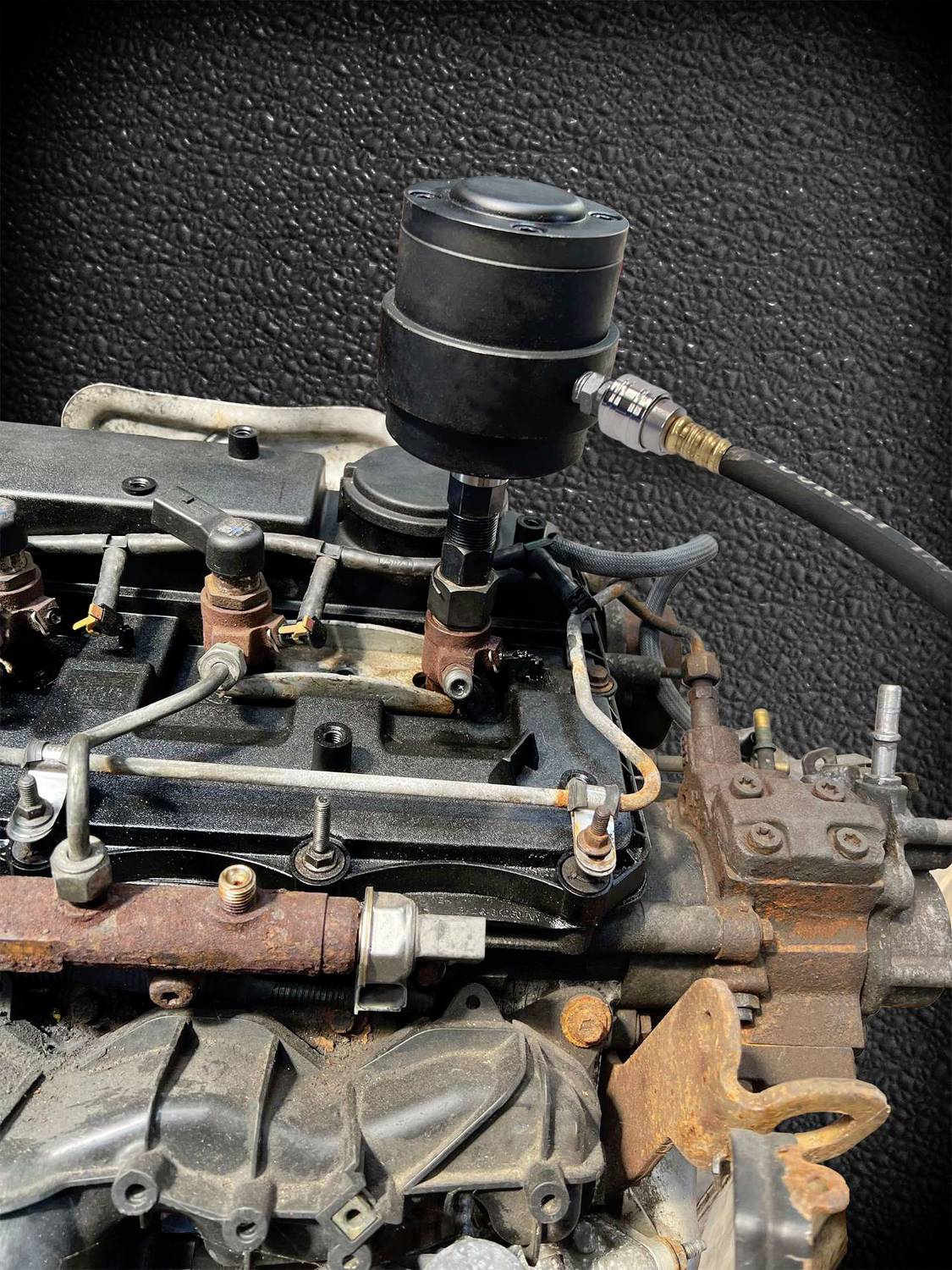 Närbild av en gammal motor med rostiga spår och en svart cylinderformad enhet ovanpå. En slangförbindelse är synlig.