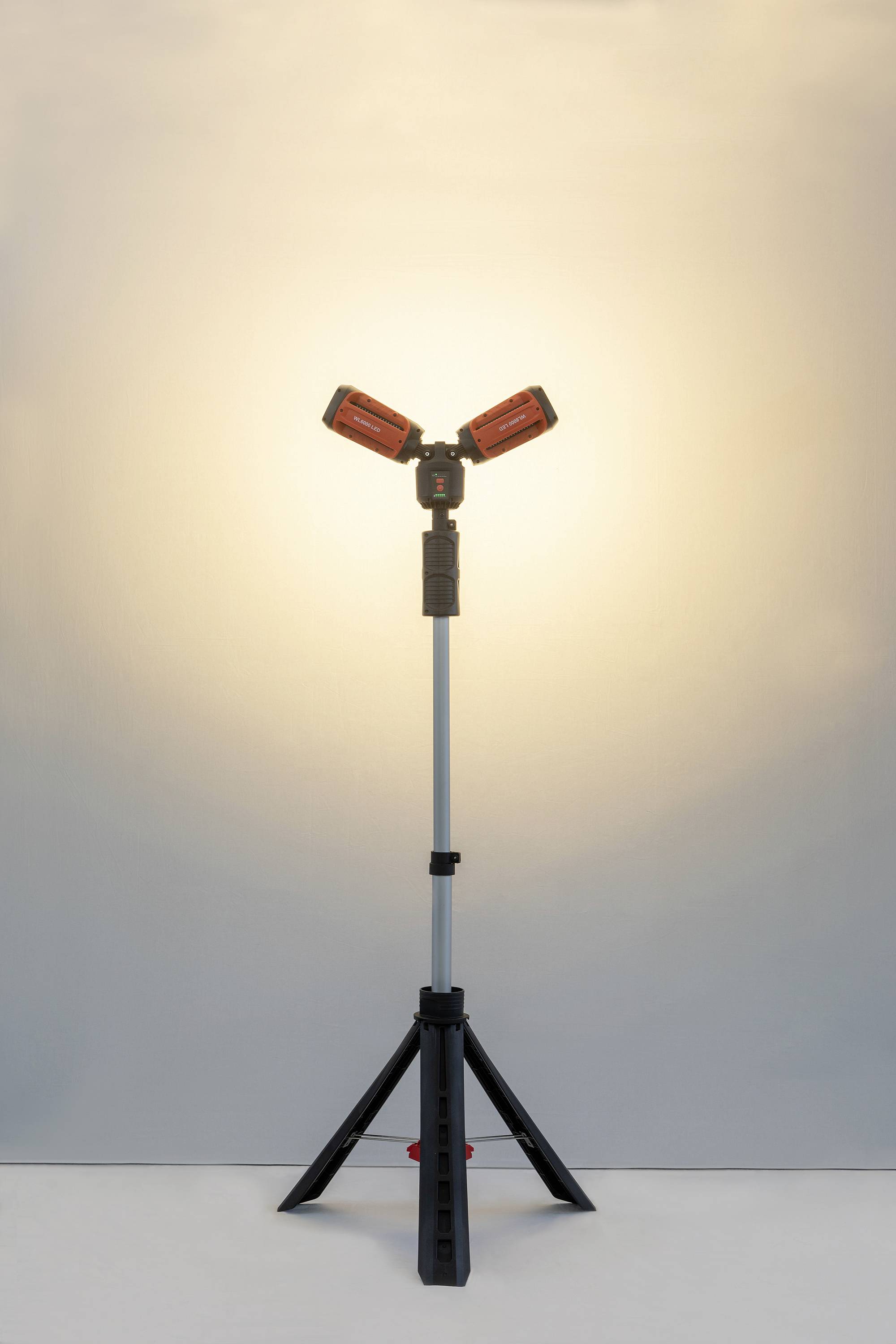 En dubbel LED-arbetslampa på ett trebent stativ lyser upp ett rum med varmt ljus, lämplig för byggprojekt.