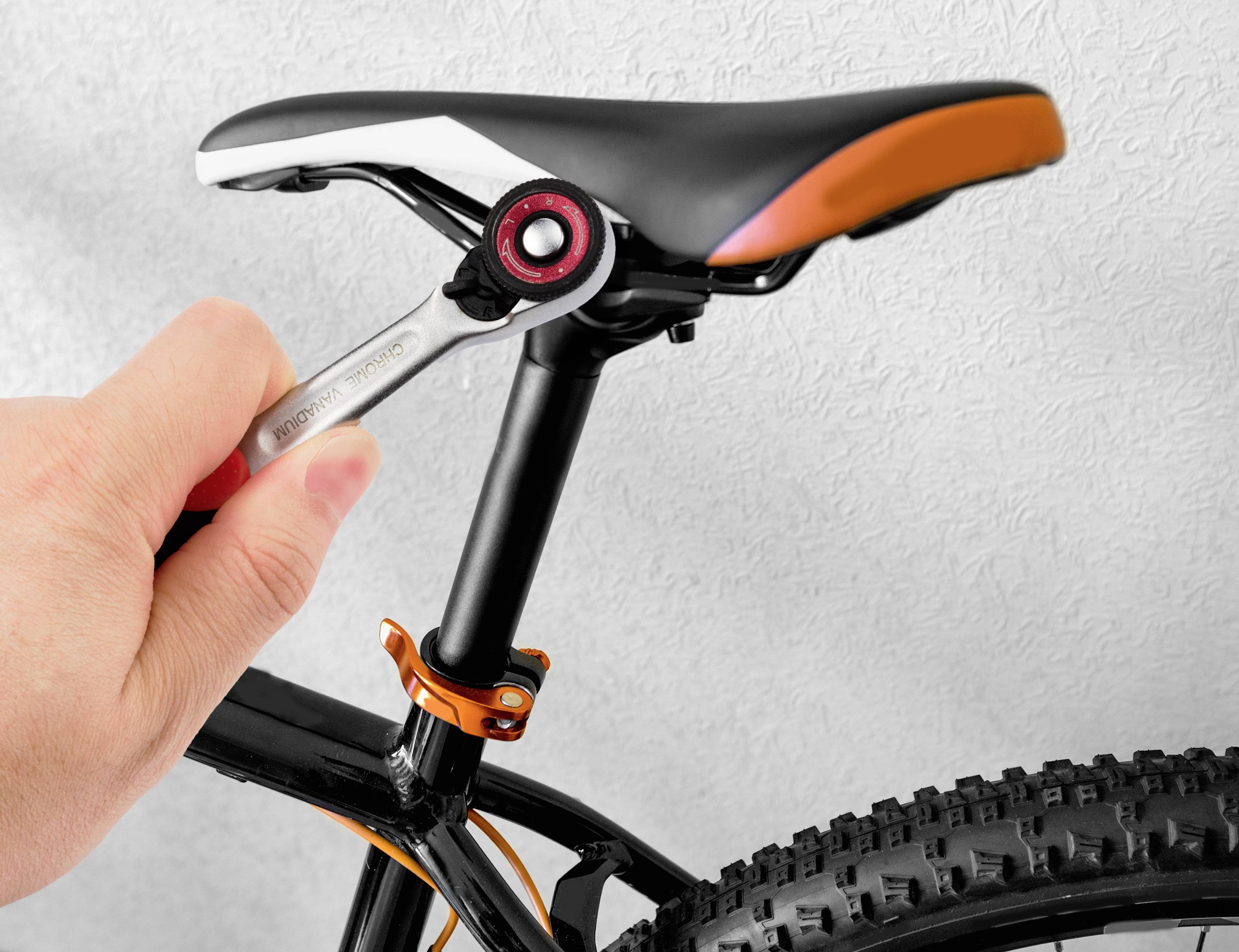 En hand drar åt sadelklämman på en cykel med en skiftnyckel. Cykeln har grova, profillösa däck och en svart ram.