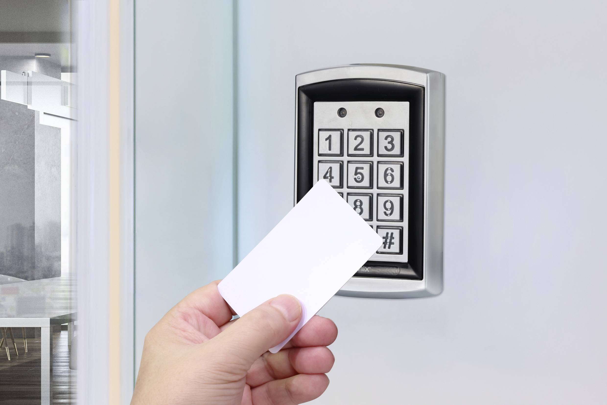En hand håller ett kort framför ett elektroniskt accesskontrollsystem med numeriskt tangentbord vid en glasdörr.