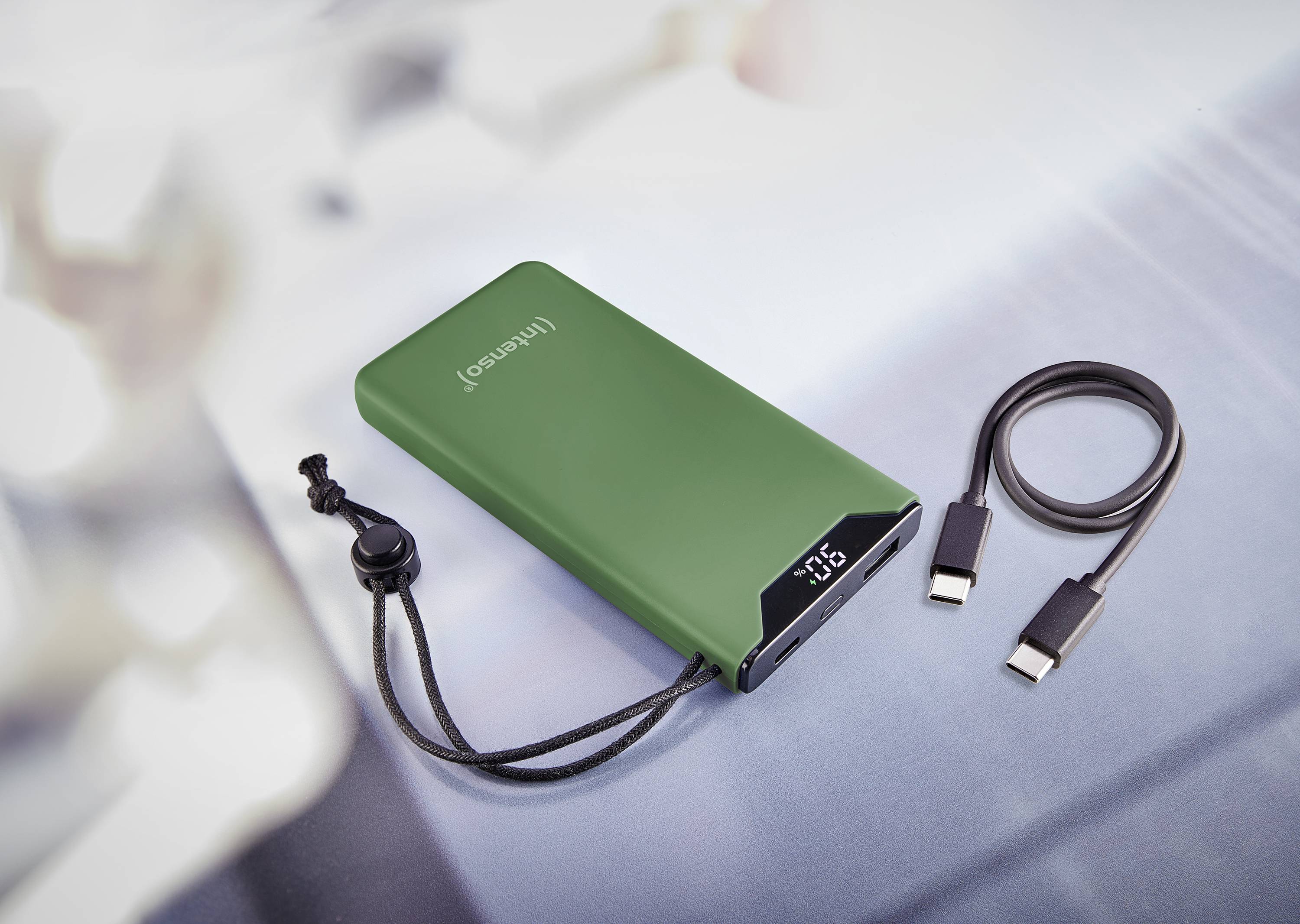 Grön powerbank med digital display för batterinivå, åtföljd av ett USB-laddningskabel på en grå yta.
