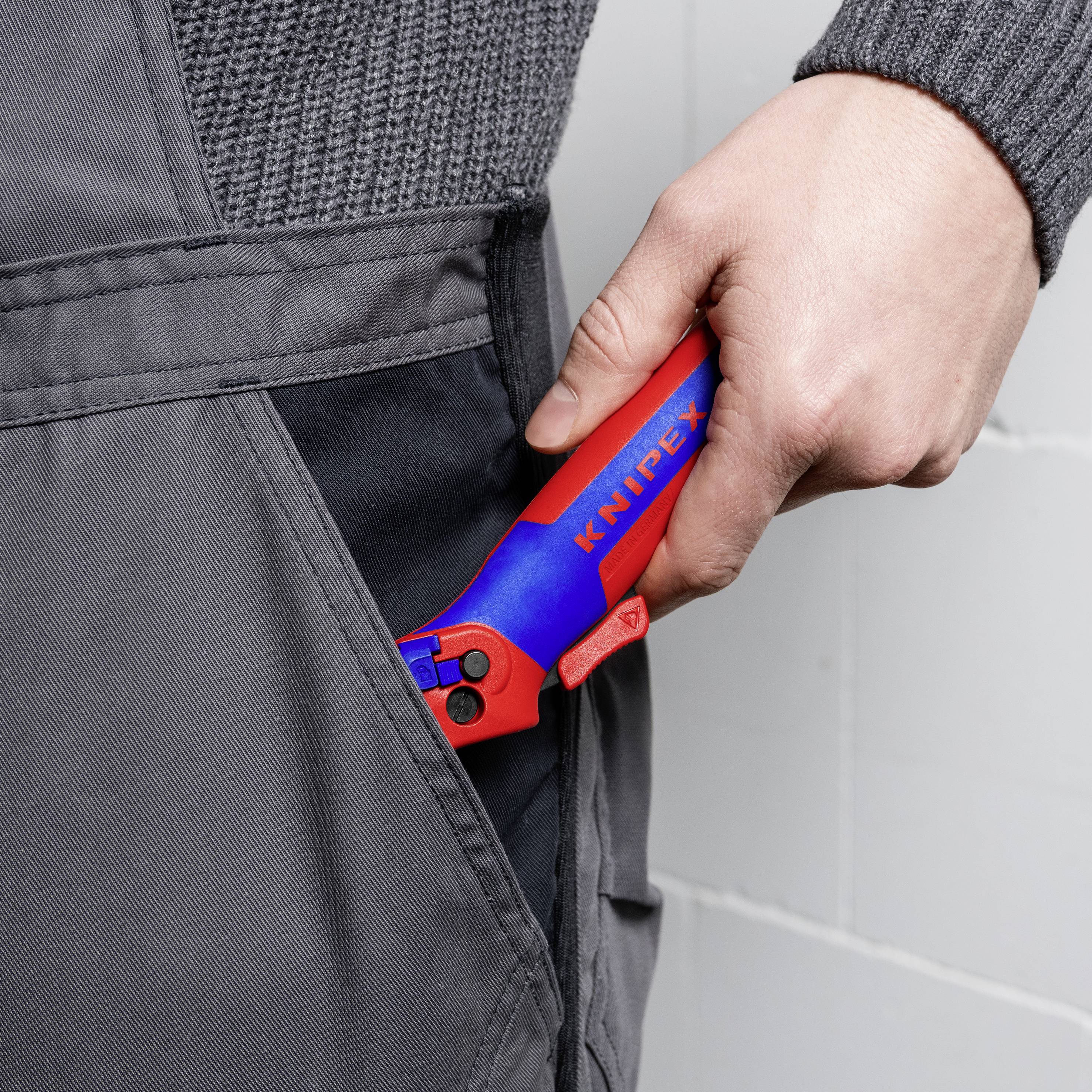 En person stoppar ett rött och ett blått verktyg märkt 'KNIPEX' i sidofickan på ett par gråa arbetsbyxor.