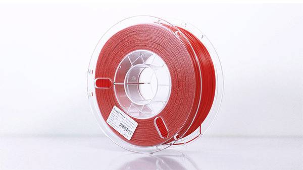 En rulle röd filament för 3D-utskrift, liggande på ett bord, visar materialtyp och tillverkaretikett på förpackningen.