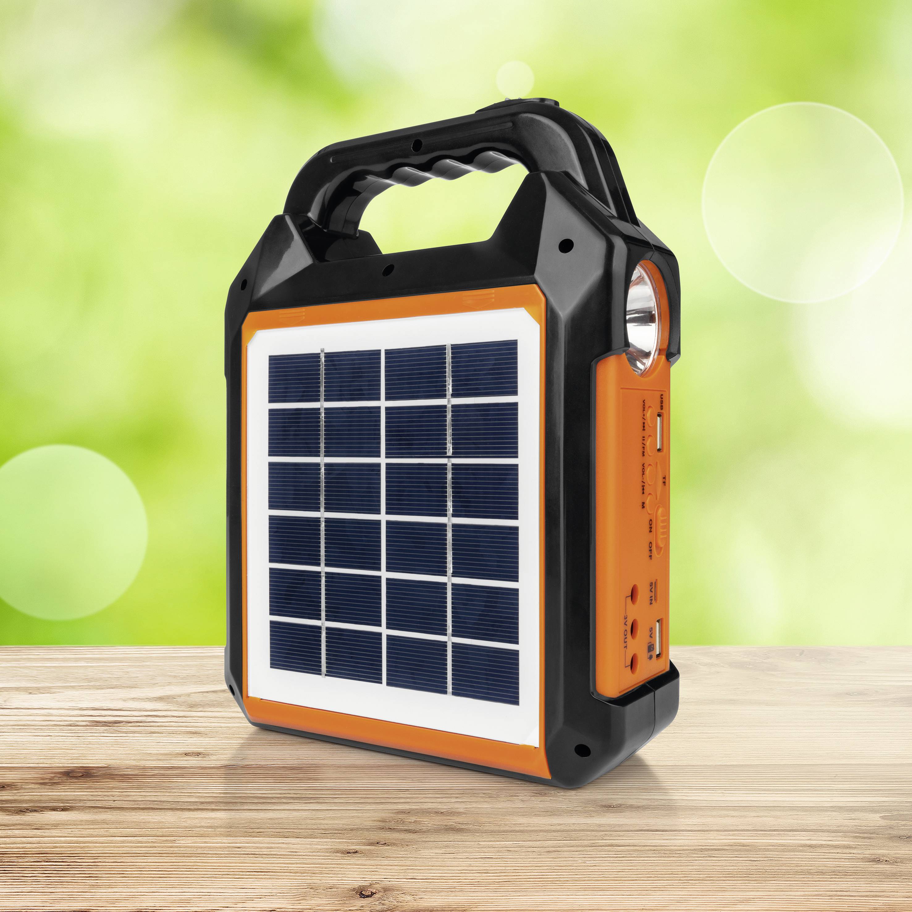 Bärbar orange-svart sollampa på ett träbord, med solceller på framsidan och en USB-port på sidan, framför en grön, suddig bakgrund.