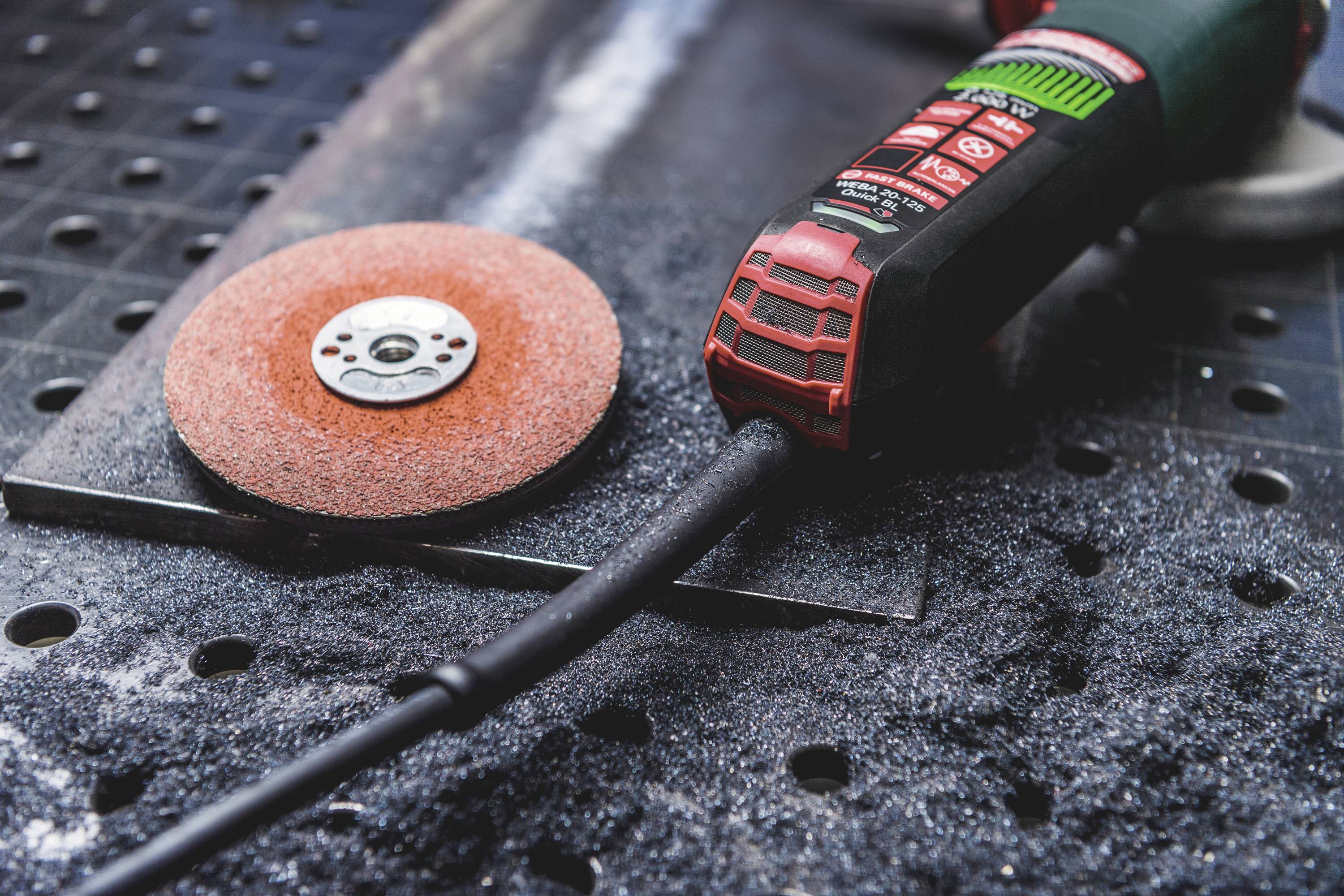Slipmaskin på en arbetsbank med en slipskiva bredvid, omgiven av metallspån. Verktyg för metallbearbetning eller -reparation.