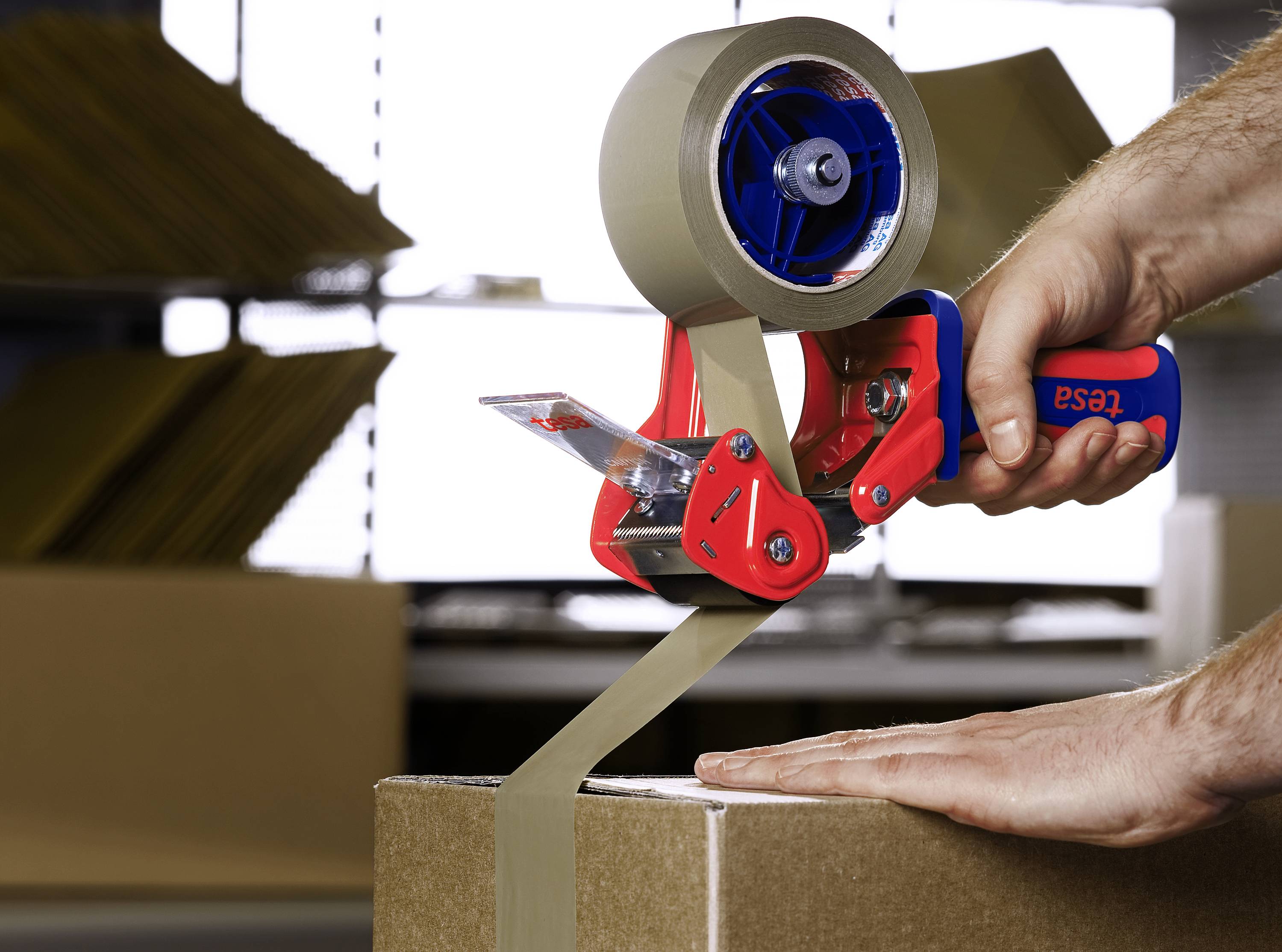 En person använder en tejpapparat för att försluta ett paket med tejp, framför en bakgrund med kartonger.