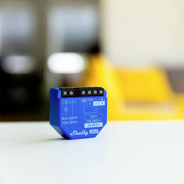 En blå Smart Home-switch från 'Shelly 2.0' med olika effekt- och spänningsspecifikationer ligger på ett vitt bord.
