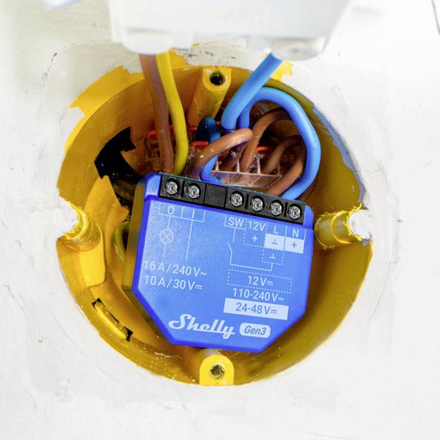 En elektrisk apparat, monterad i ett vägguttag, kabelansluten med olika färgade ledningar, visar spänningsdata: '16A/240V'.