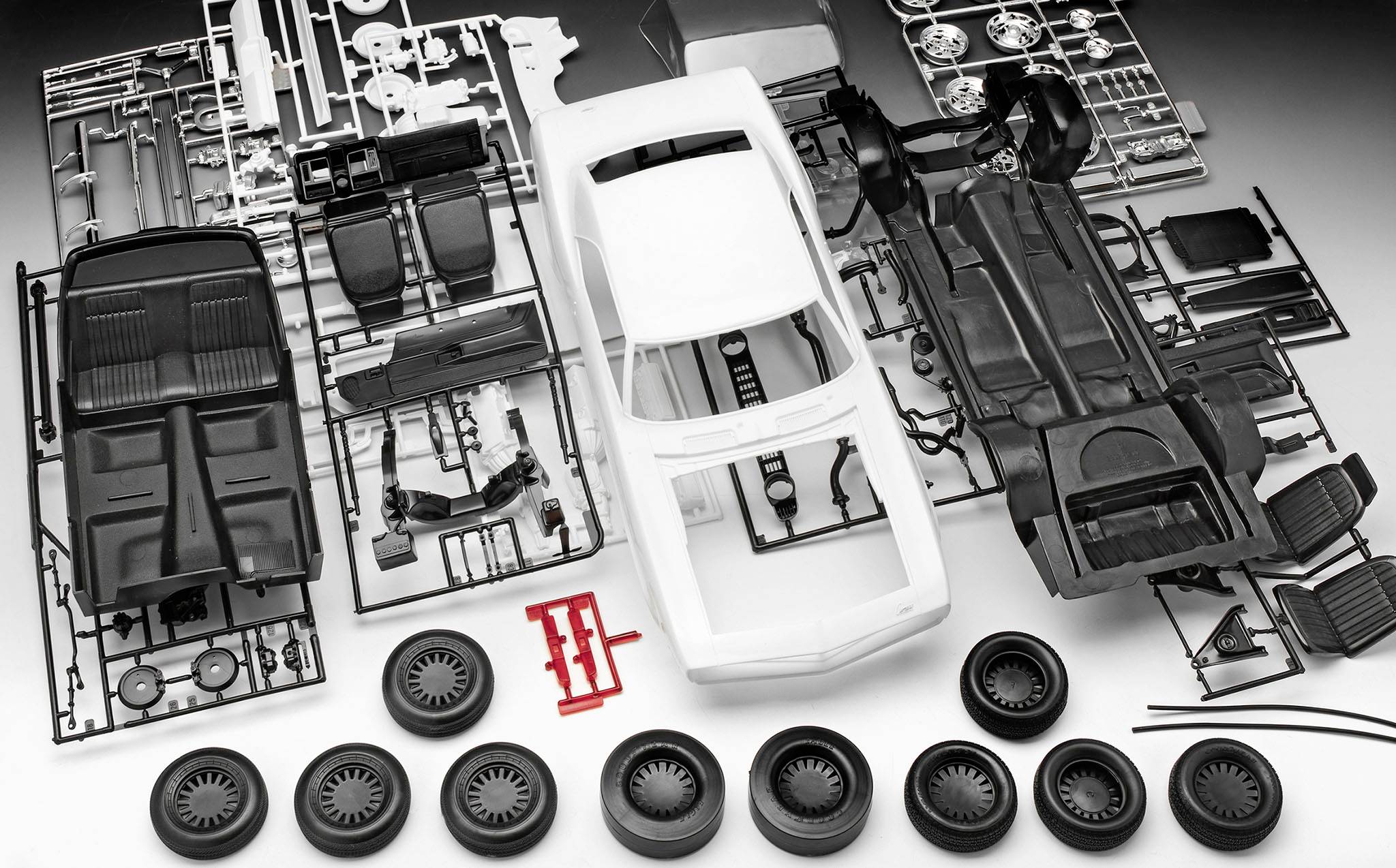 Plastdelar från en modelbil i lösa delar, inklusive kaross, hjul och tillbehör, placerade på en grå yta.