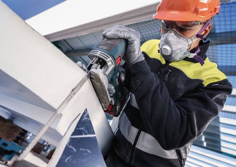 Arbetar sågar metall med skyddskläder och hjälm i industriell miljö.