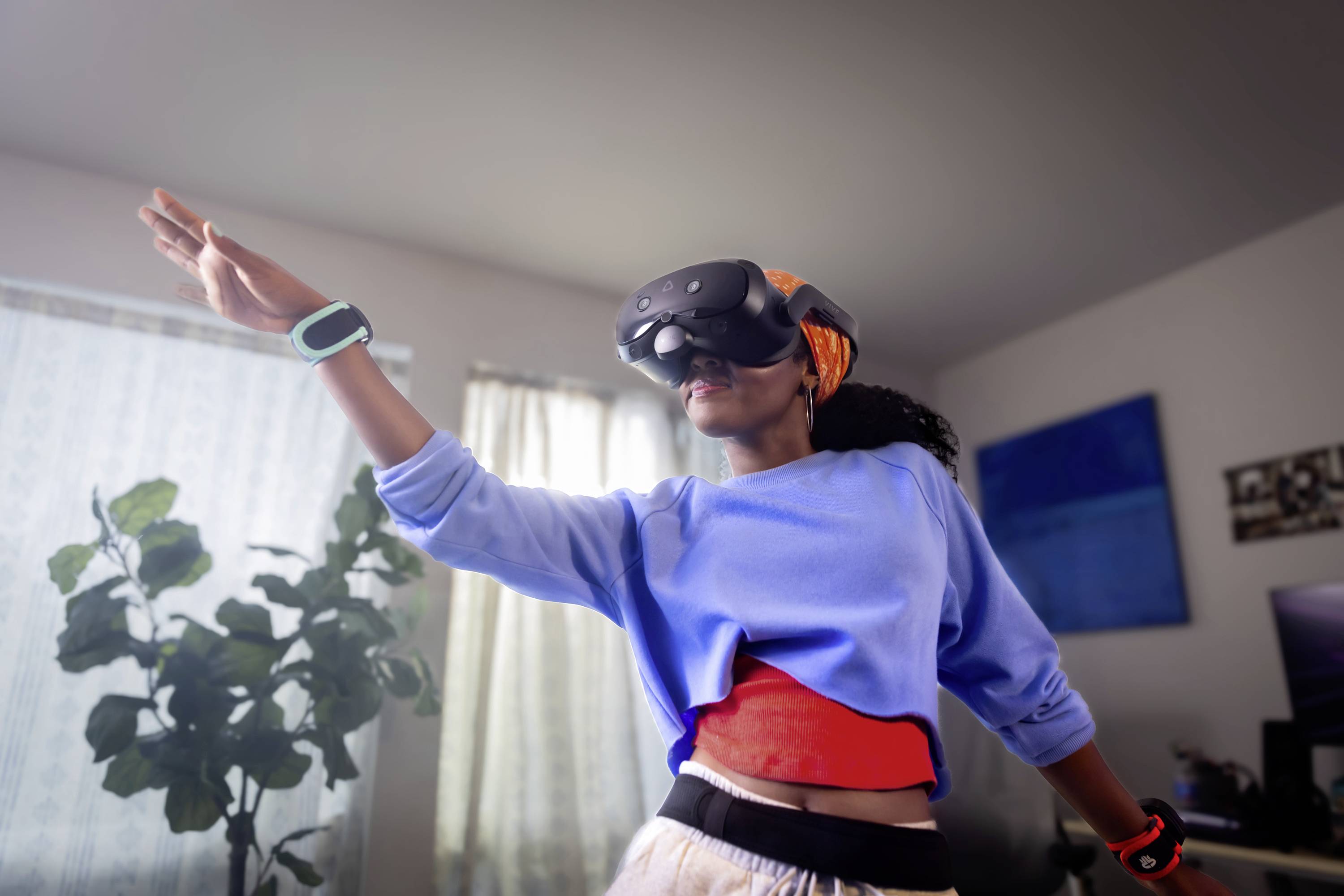 En person med VR-glasögon dansar i ett rum, bär ett orange pannband och ett blått överdel; rörelse betonas.