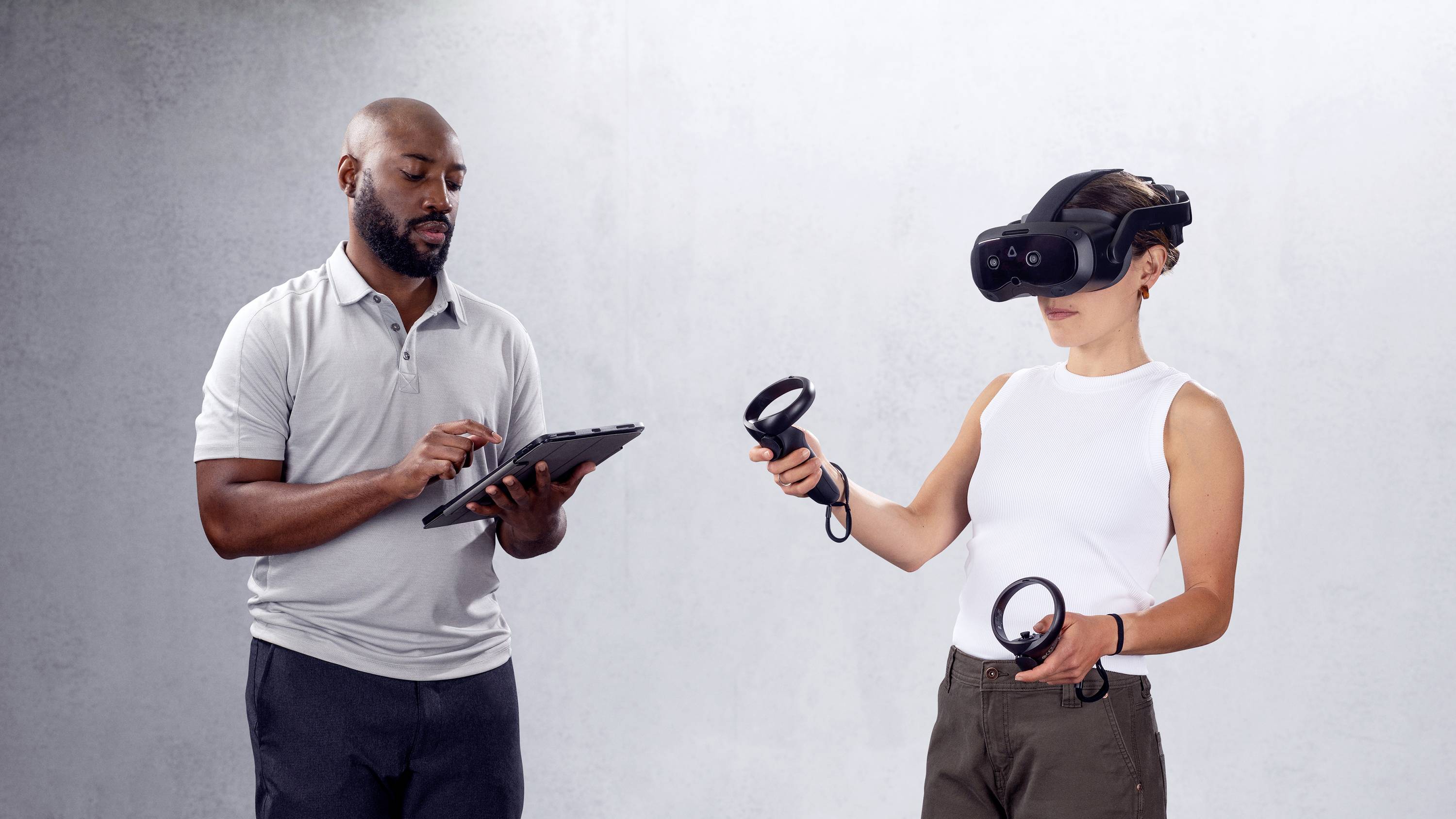 En man tittar på en surfplatta medan en kvinna bär ett Virtual Reality-headset och handkontroller.