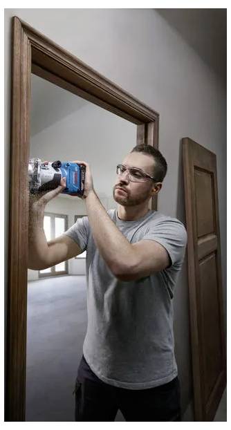 En man använder en trådlös borrmaskin för att installera eller reparera ett trädörrkarm inomhus.