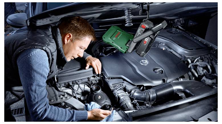 En mekaniker inspekterar en bilmotor i en öppen motorhuv och använder ett diagnostikverktyg under motorkupeén.