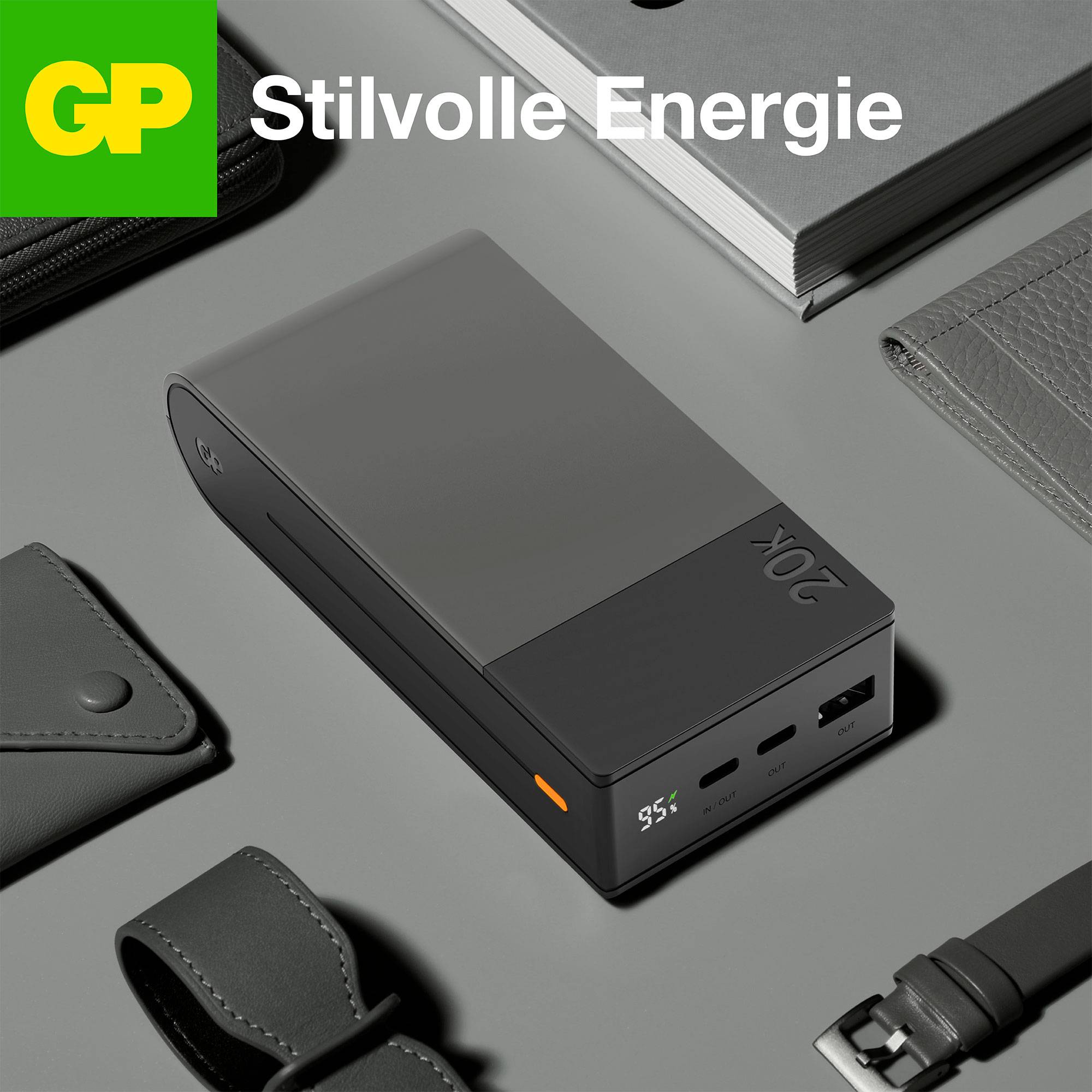 En powerbank med digital display och två USB-portar ligger stilfullt på ett bord bredvid en läderkasse och en anteckningsbok.