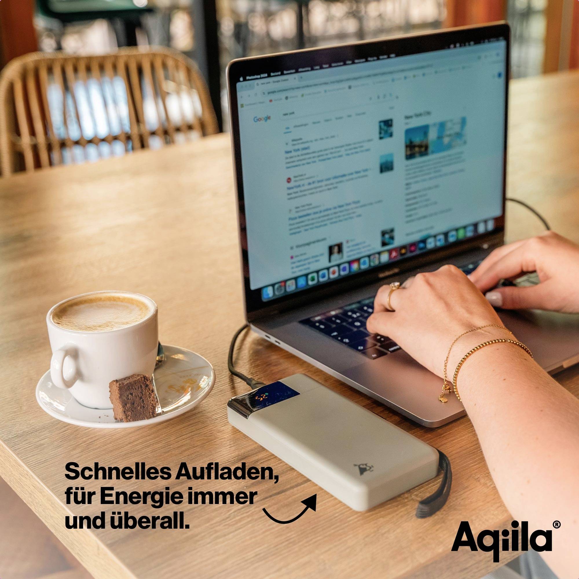 En person arbetar på en laptop i ett café, bredvid en kopp kaffe och en bit kaka på ett träbord. En laddare laddar en enhet. Text: 'Snabb laddning, för energi när som helst och överallt.'