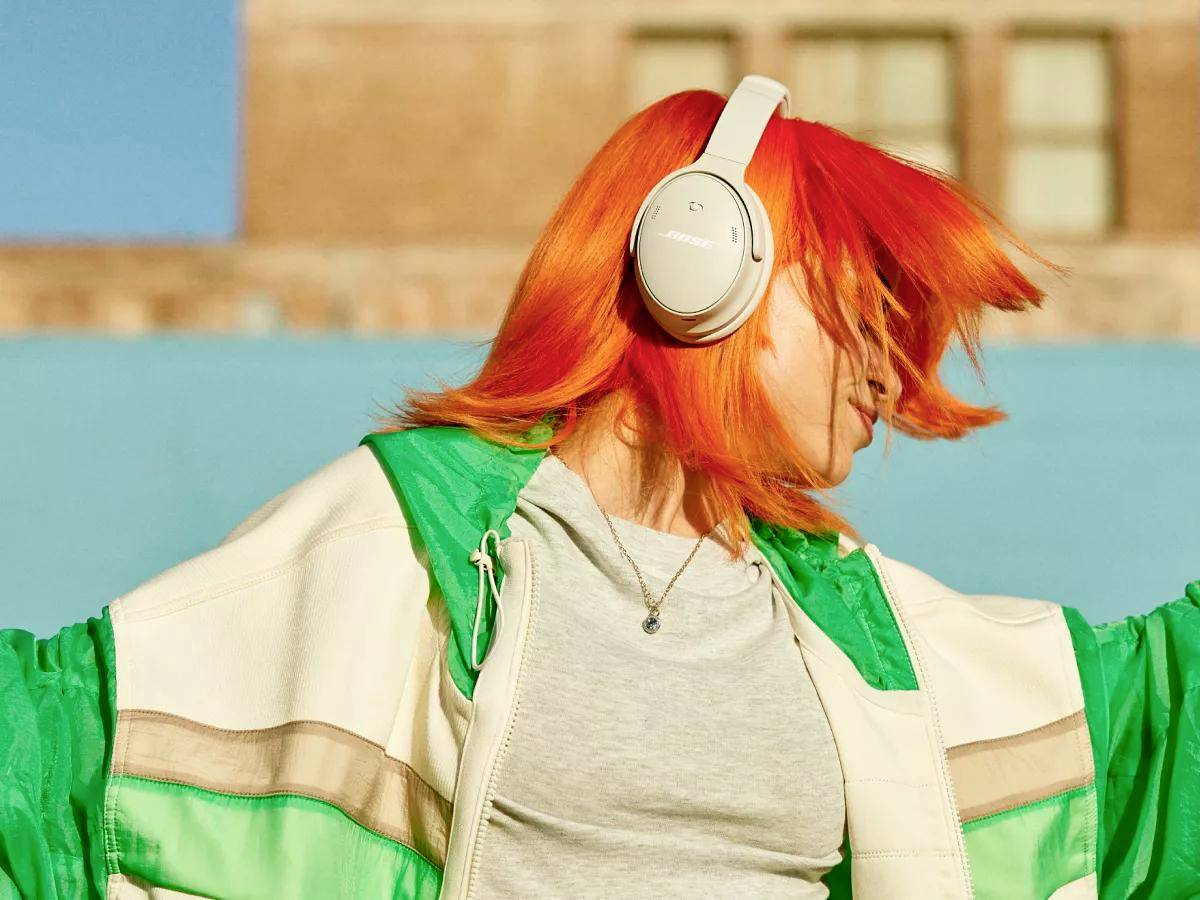 En person med lysande orange hår har hörlurar på sig och rör sig till musiken framför en klarblå himmel.