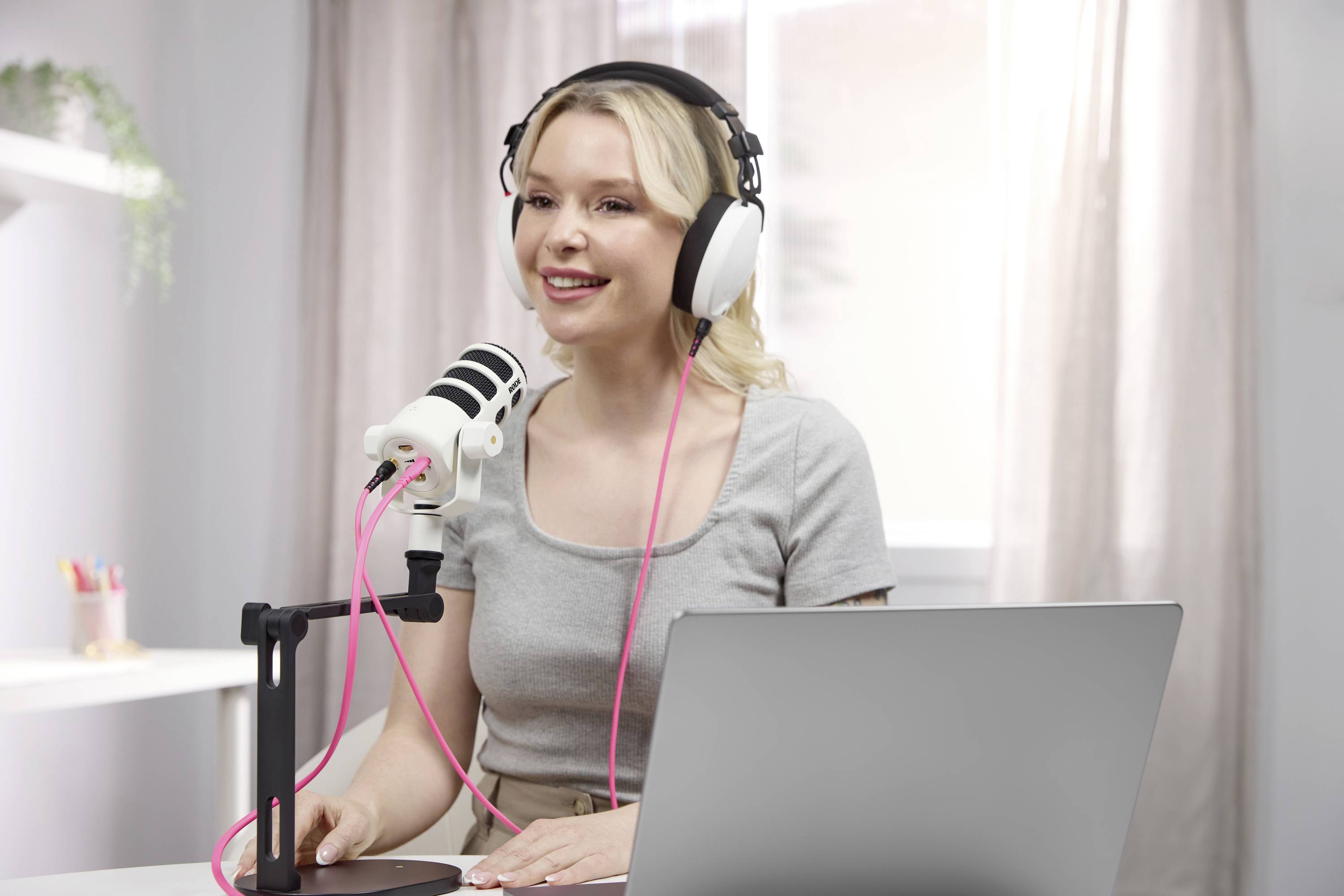 En kvinna sitter vid ett bord framför en mikrofon med hörlurar och en bärbar dator, som om hon spelar in en podcast eller en inspelning.