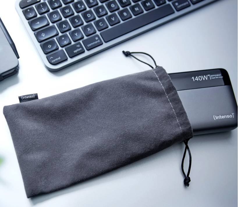 Extern hårddisk 'Intenso' med 140 W effekt ligger delvis i en grå påse; bredvid finns ett tangentbord på ett bord.